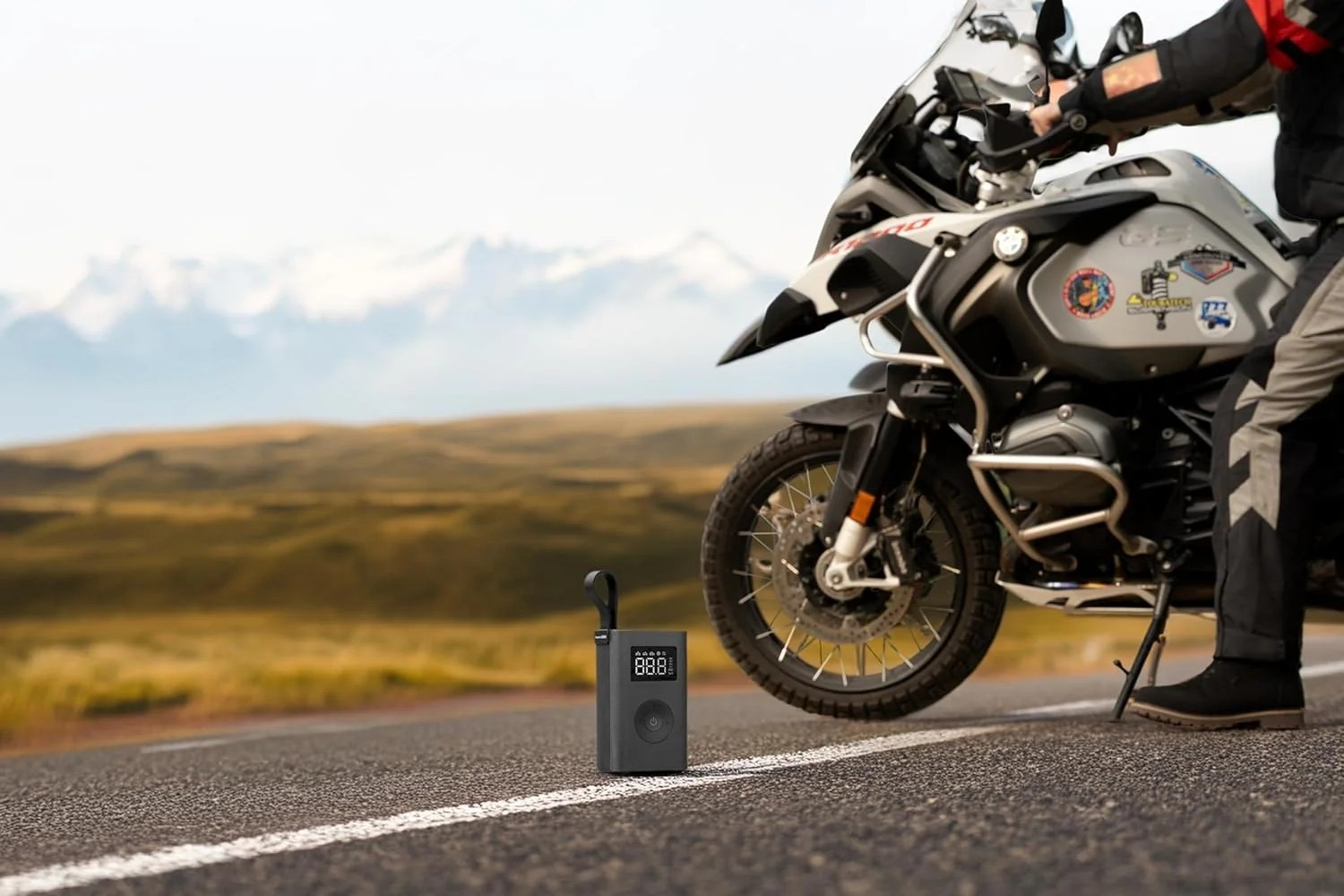 Ein Motorrad steht auf einer Straße mit einem Reifenfüller daneben, Berge im Hintergrund.