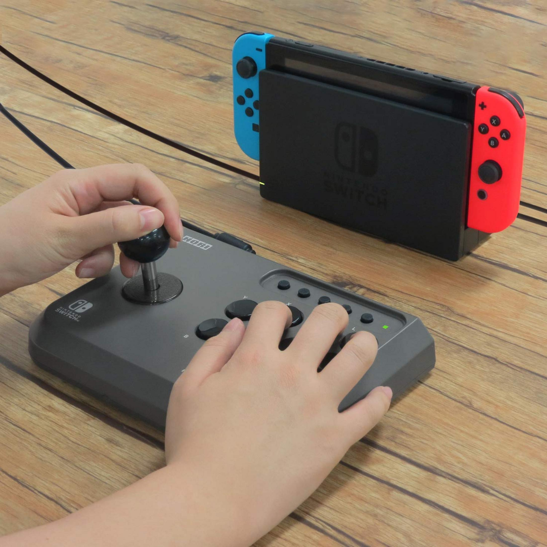Osoba gra w Nintendo Switch z Hori arcade stick na drewnianym stole.