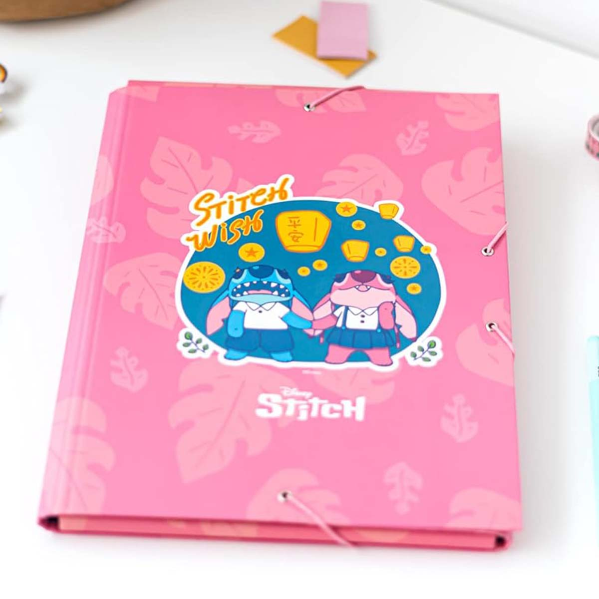 Pinkes Notizbuch mit Stitch und Angel, die sich unter Laternen an den Händen halten.