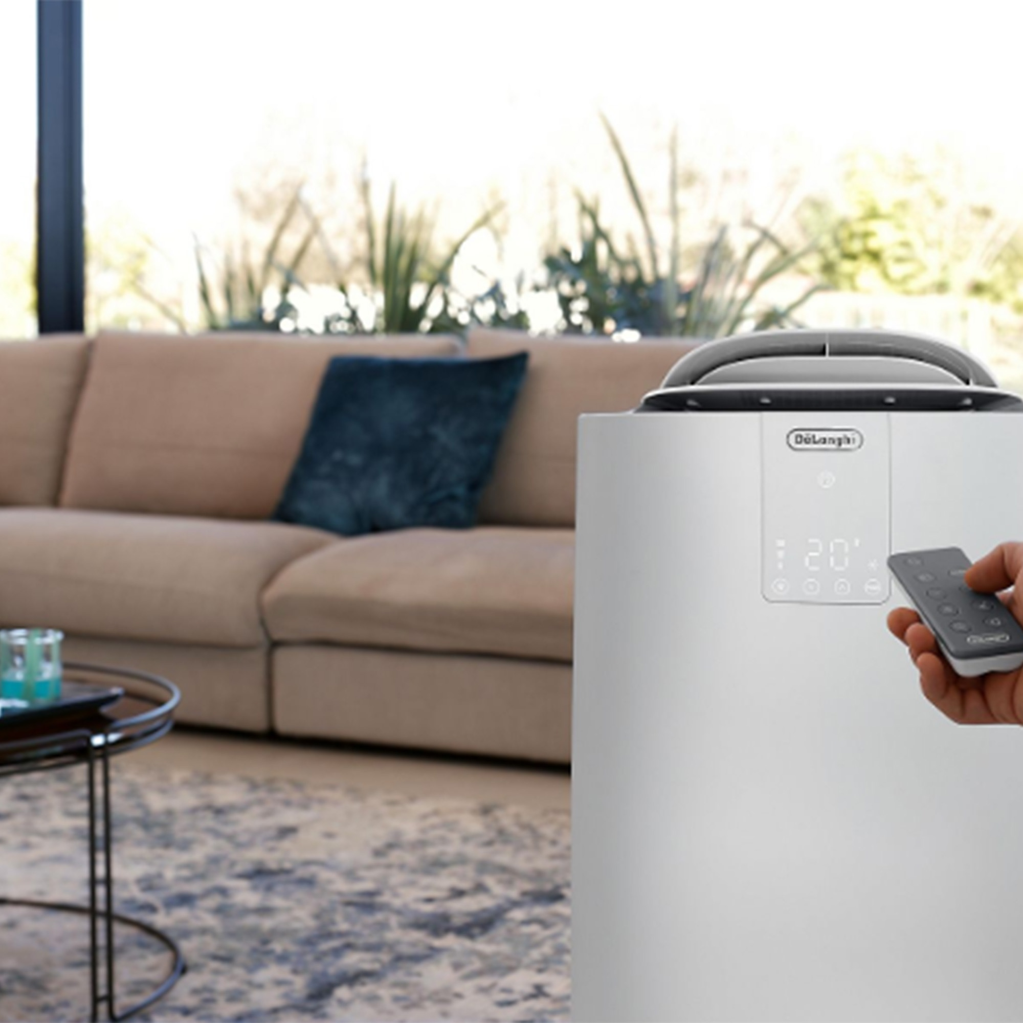 Ein DeLonghi-Luftkühler mit Fernbedienung in einem Wohnzimmer mit Sofa.