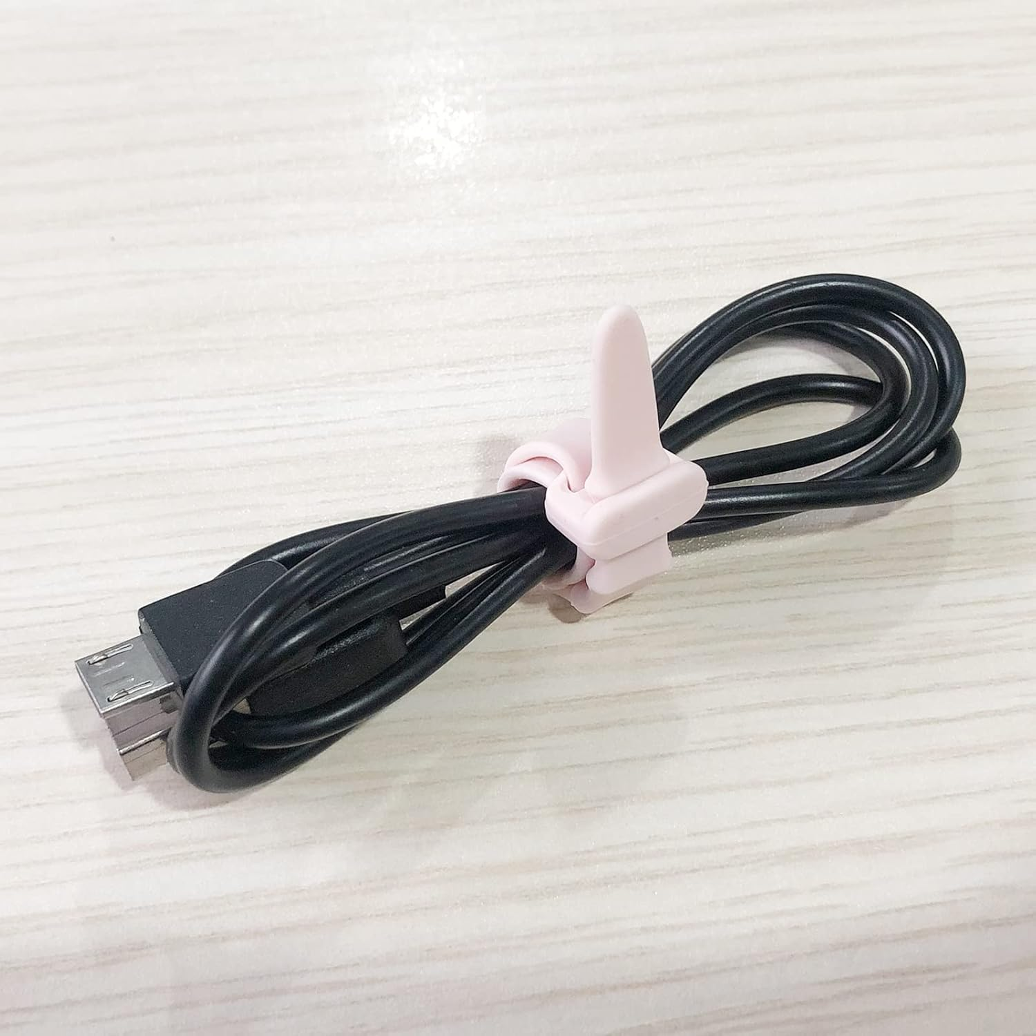 Ein rosa Kabelhalter hält ein schwarzes USB-Kabel auf einem Holztisch.