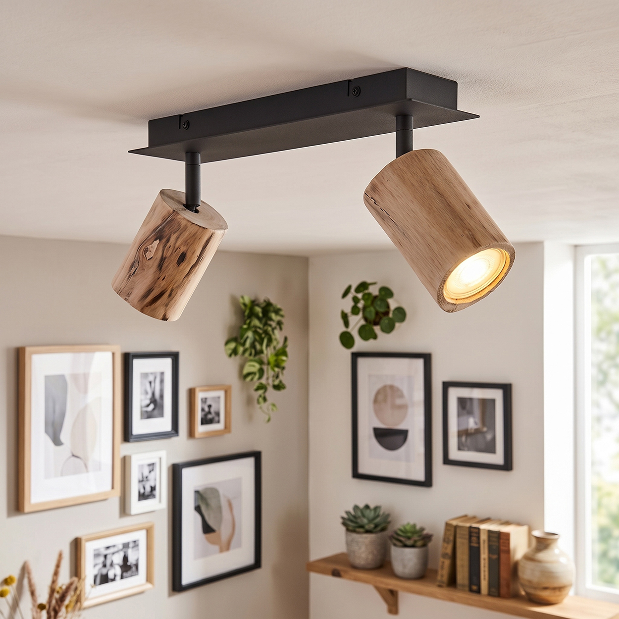 Eine Deckenleuchte mit zwei zylindrischen Holzstrahlern an einer schwarzen Stange. Bilder hängen an der Wand.