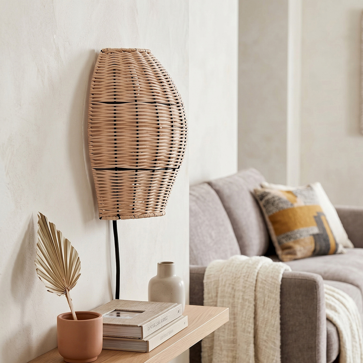 Geflochtene Wandlampe über Regal mit Büchern, Vase und getrocknetem Palmenblatt. Sofa im Hintergrund.