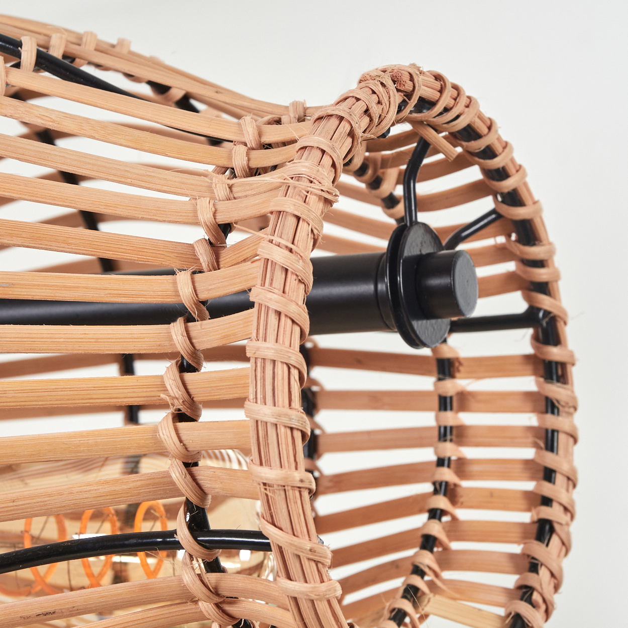 Nahaufnahme einer runden Lampe aus geflochtenem Rattan mit schwarzem Metallgestell.