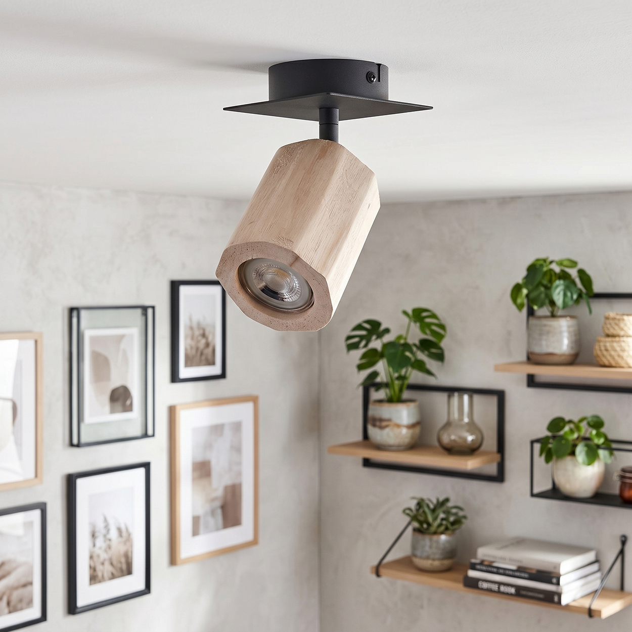 Ein hölzerner Deckenstrahler mit schwarzer Halterung ist nach unten gerichtet. Die Wand hat gerahmte Bilder und Regale mit Pflanzen.