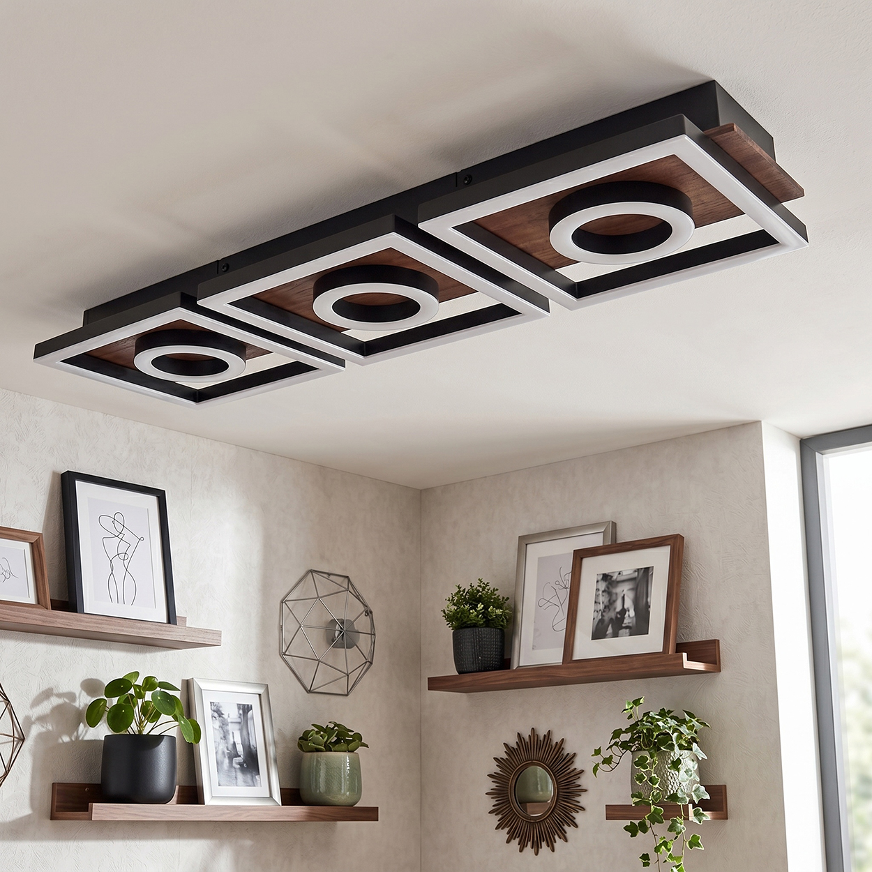 Moderne Deckenleuchte mit Holz, Metall und LED-Ringen über Bilderrahmen und Pflanzen.