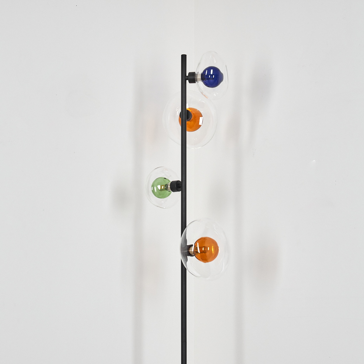 Ein dunkler Lampenständer mit vier Glaskugeln, die blaue, orange und grüne Lichter enthalten.