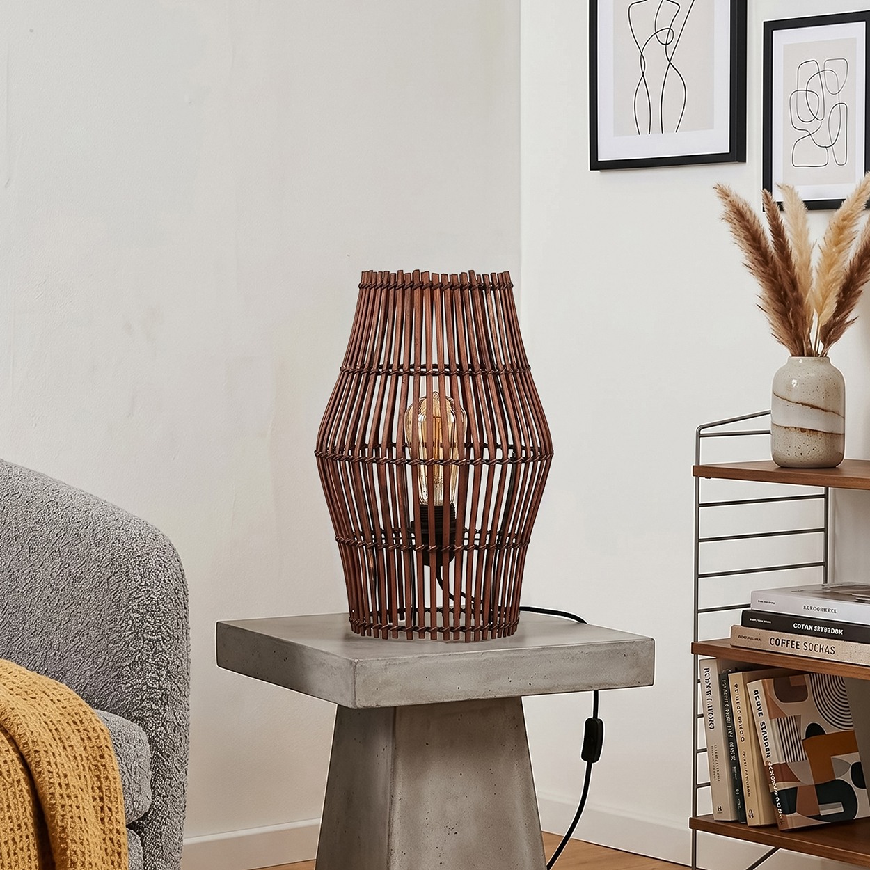 Eine braune Rattanzwischenlampe mit Edison-Glühbirne steht auf einem Betontisch.
