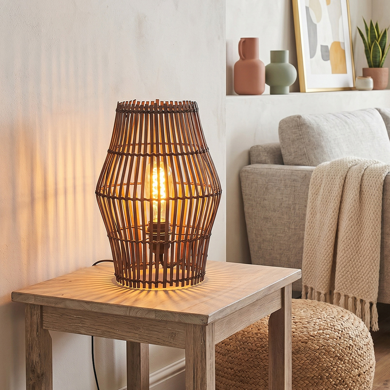Eine braune Weidenkorb-Tischlampe beleuchtet einen Holztisch. Ein Sofa mit Decke ist im Hintergrund.