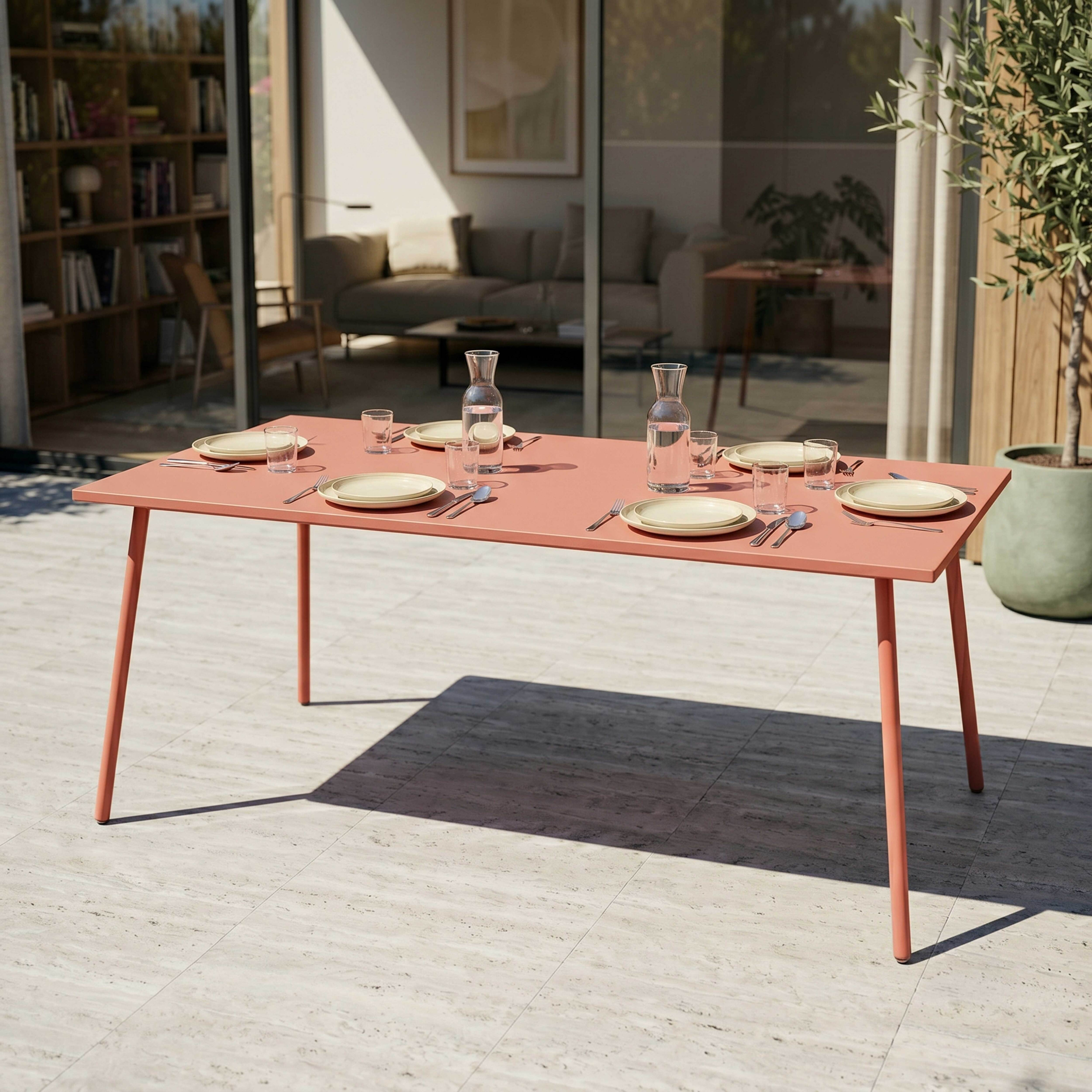 Ein korallenroter Tisch mit gedeckter Tafel steht auf einer gefliesten Terrasse.