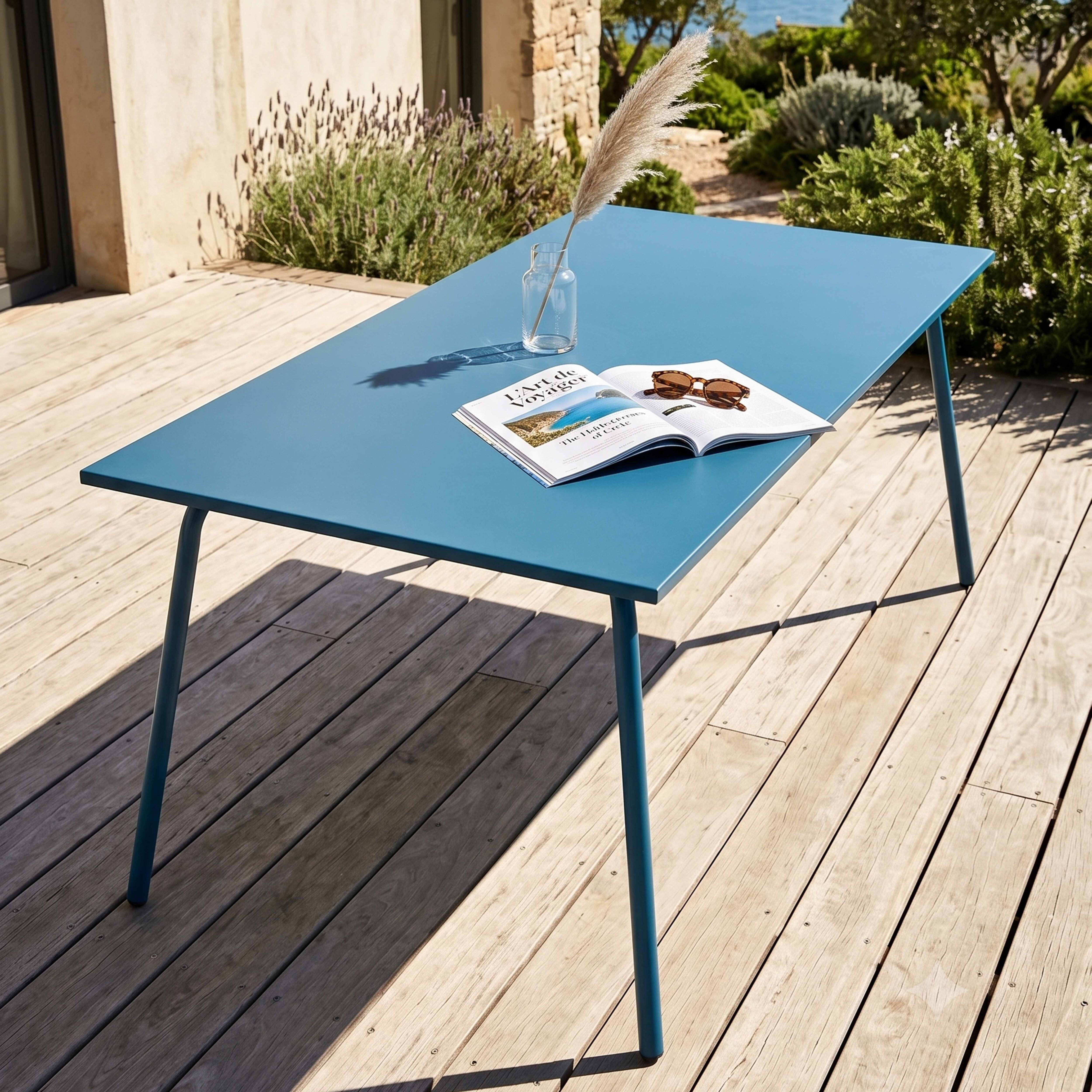 Ein blauer Tisch mit einem Buch und Sonnenbrille auf einer Holzterrasse.