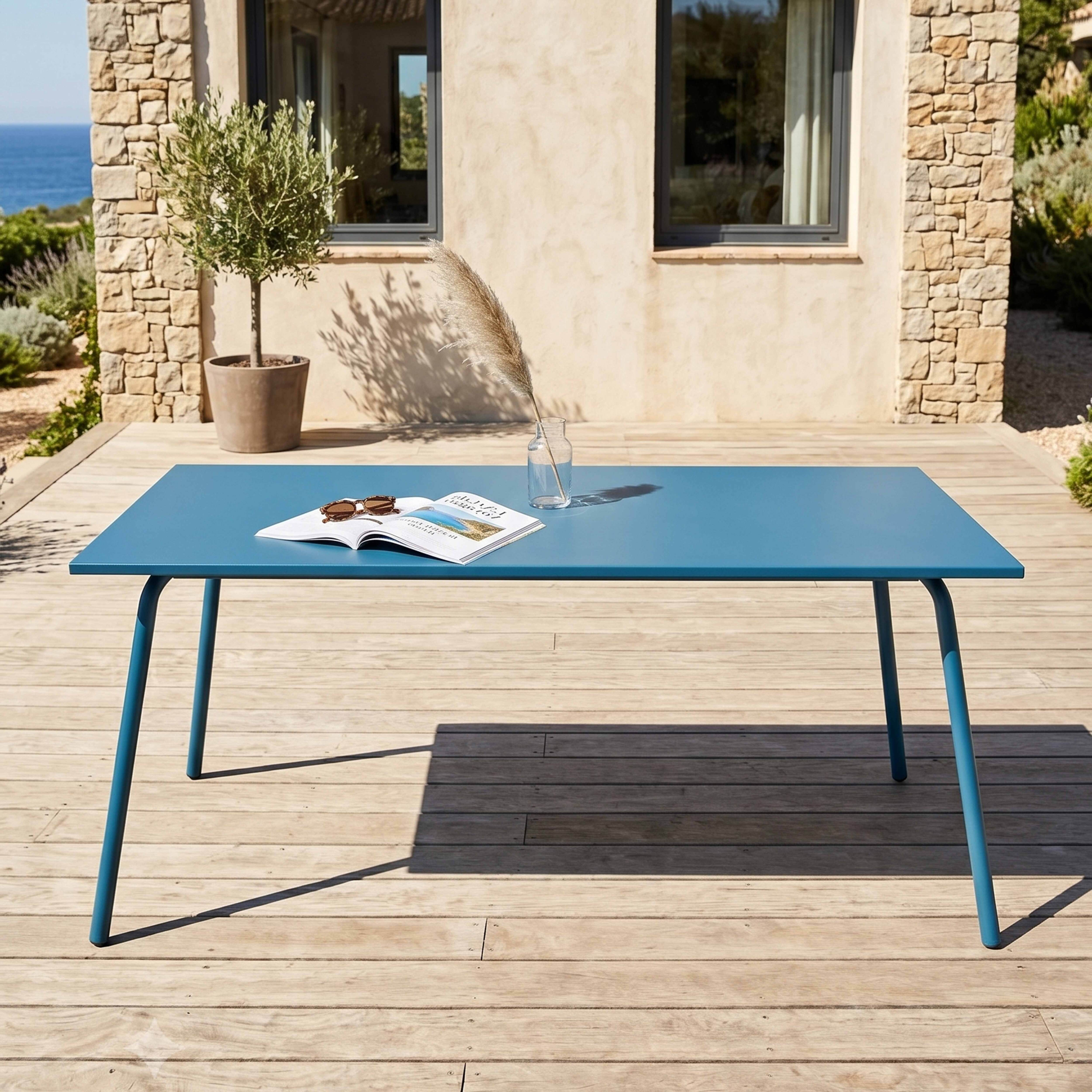 Ein blauer Tisch mit einem Buch und Sonnenbrille auf einer Holzterrasse.