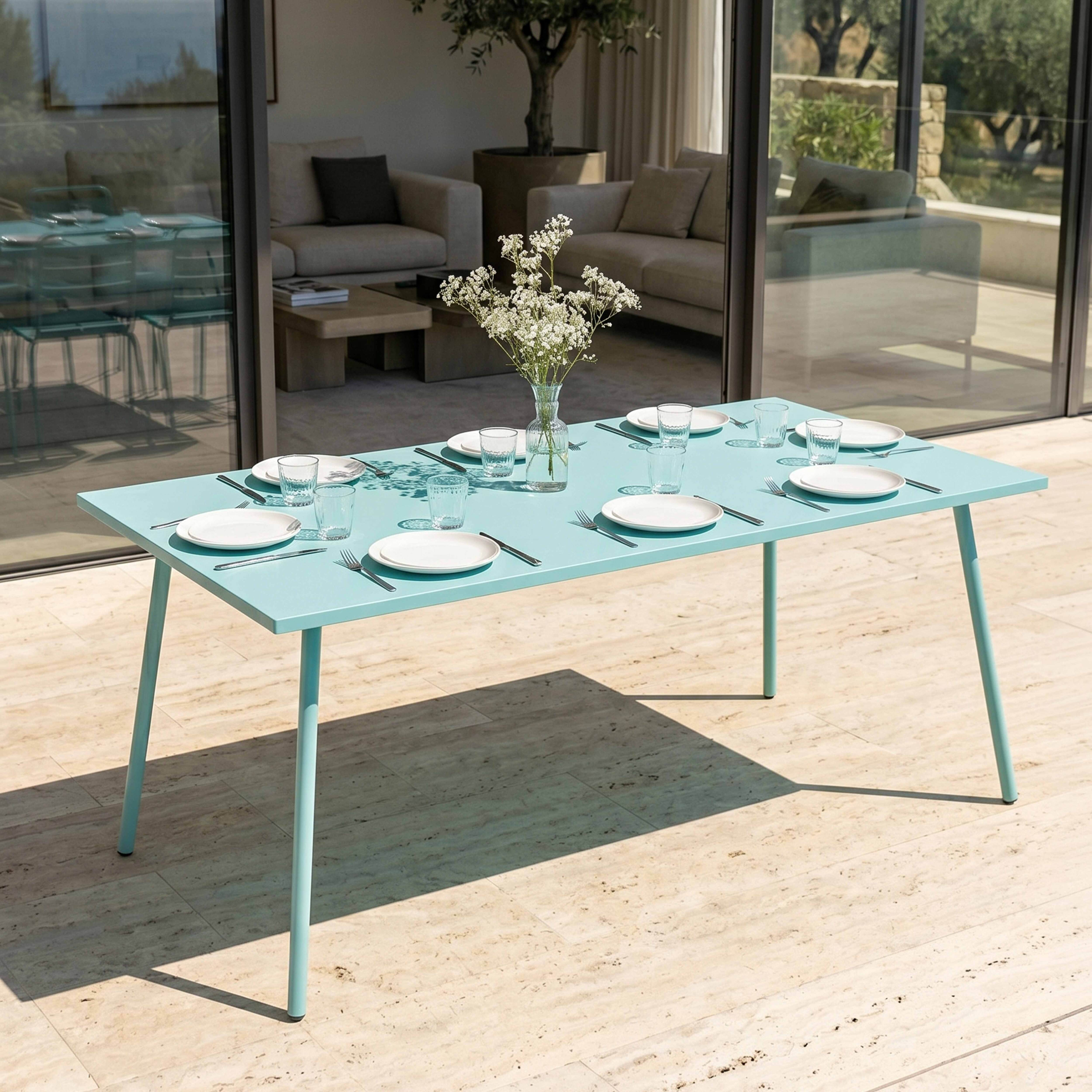 Ein hellblauer Esstisch für sechs Personen auf einer gefliesten Terrasse, mit einer Glasvase mit weißen Blumen.