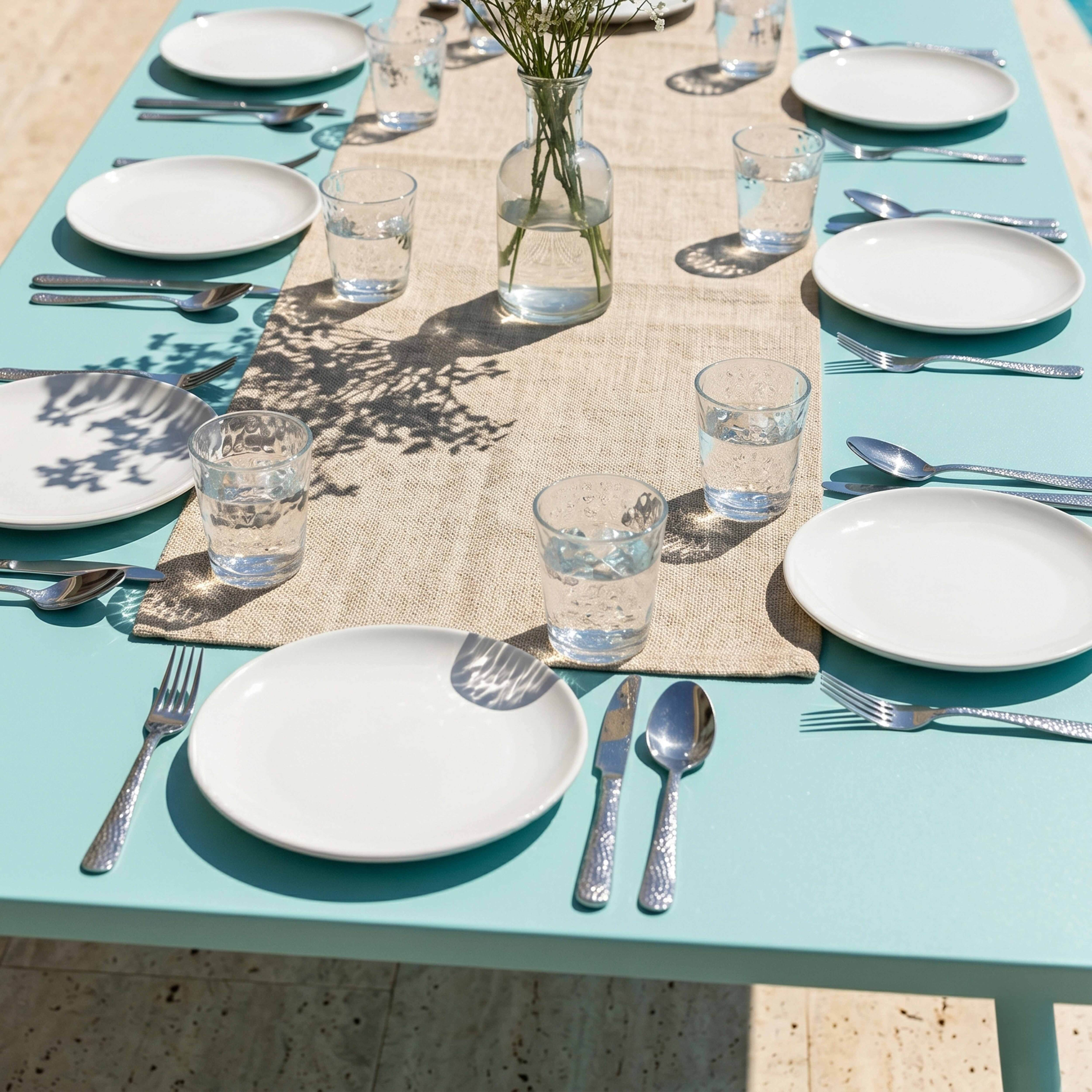Festlich gedeckter Tisch mit Tellern, Gläsern, Besteck und Blumen in Vase.