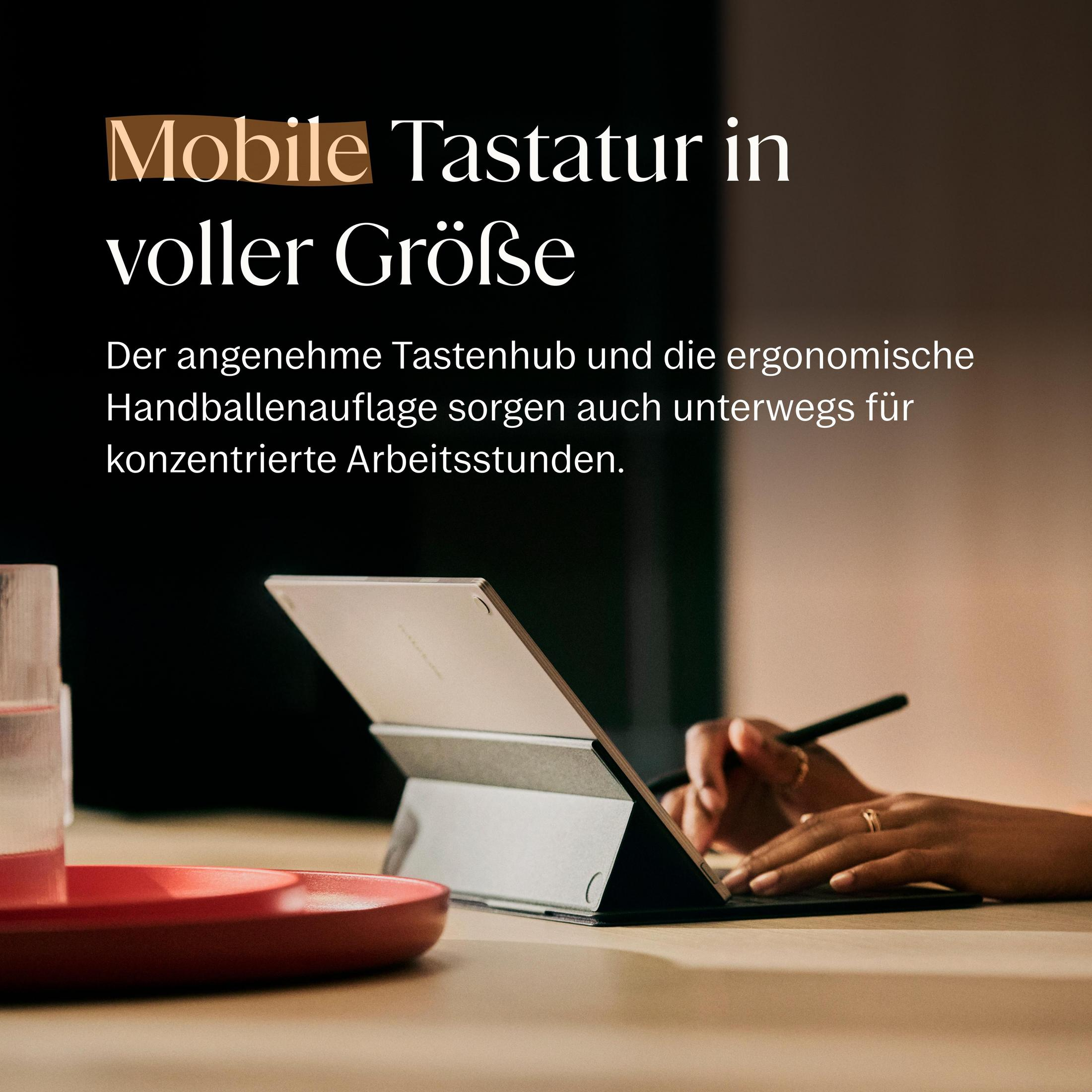 Kişi tablet ve klavyeyle çalışıyor. Önde kırmızı kase ve bardak var.