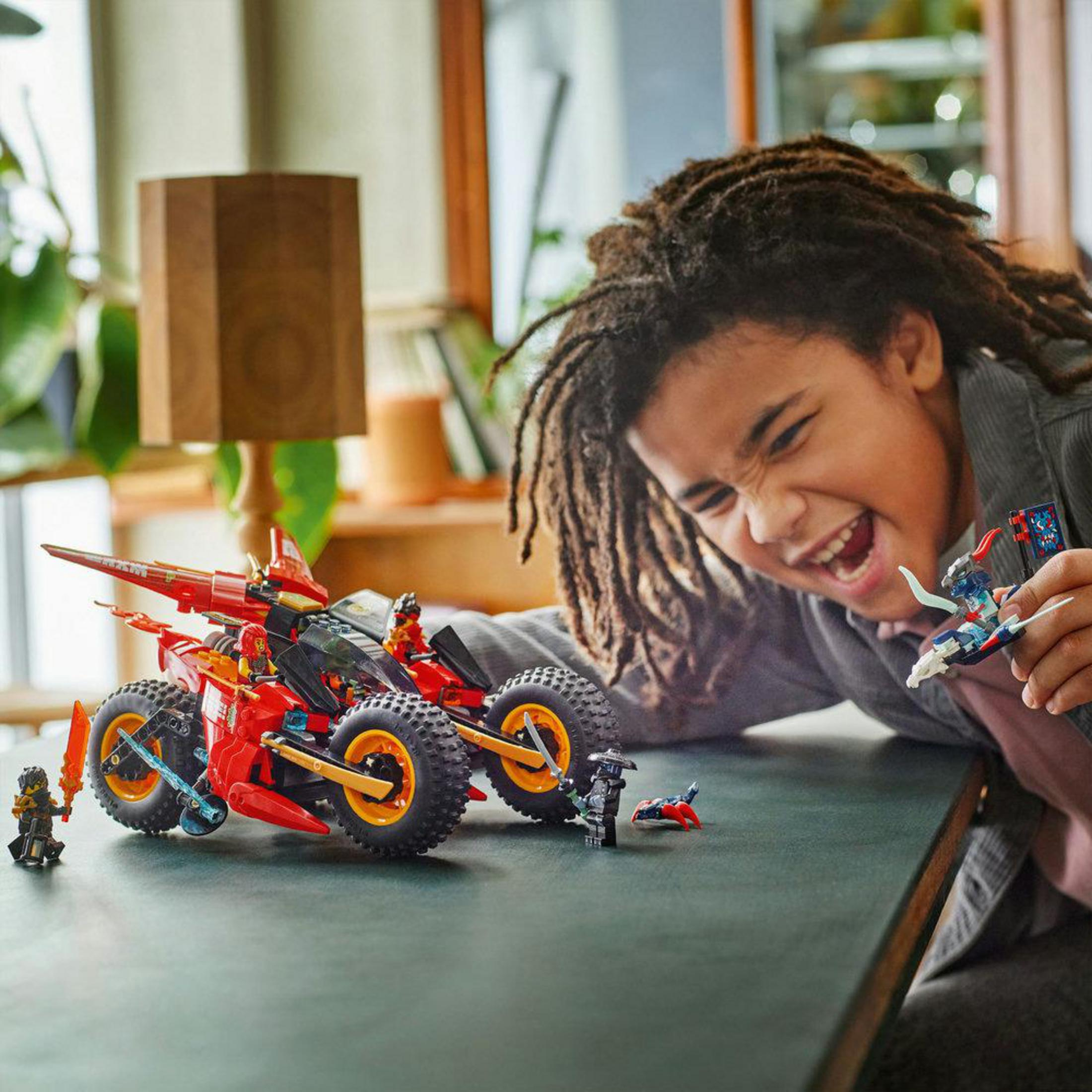 Ragazzo gioca con veicolo e figure Lego rosse su un tavolo.