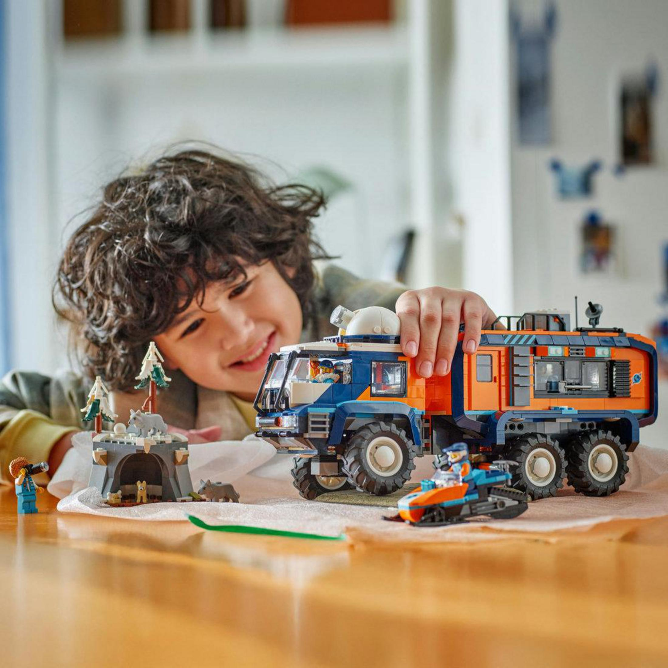 Een jongen speelt met een Lego voertuig, sneeuwscooter en poolbasis.