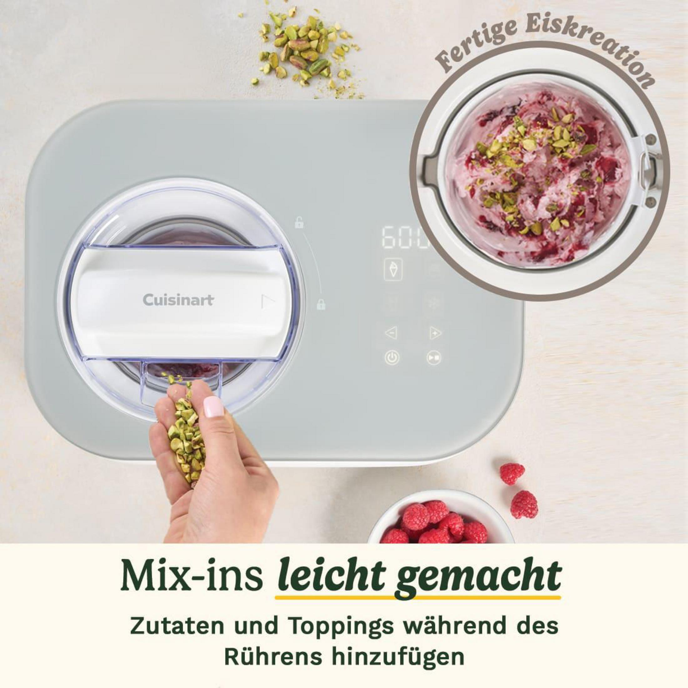 Eine hellgraue Eismaschine mit einer Hand, die Pistazien hinzufügt. Eis im Behälter.