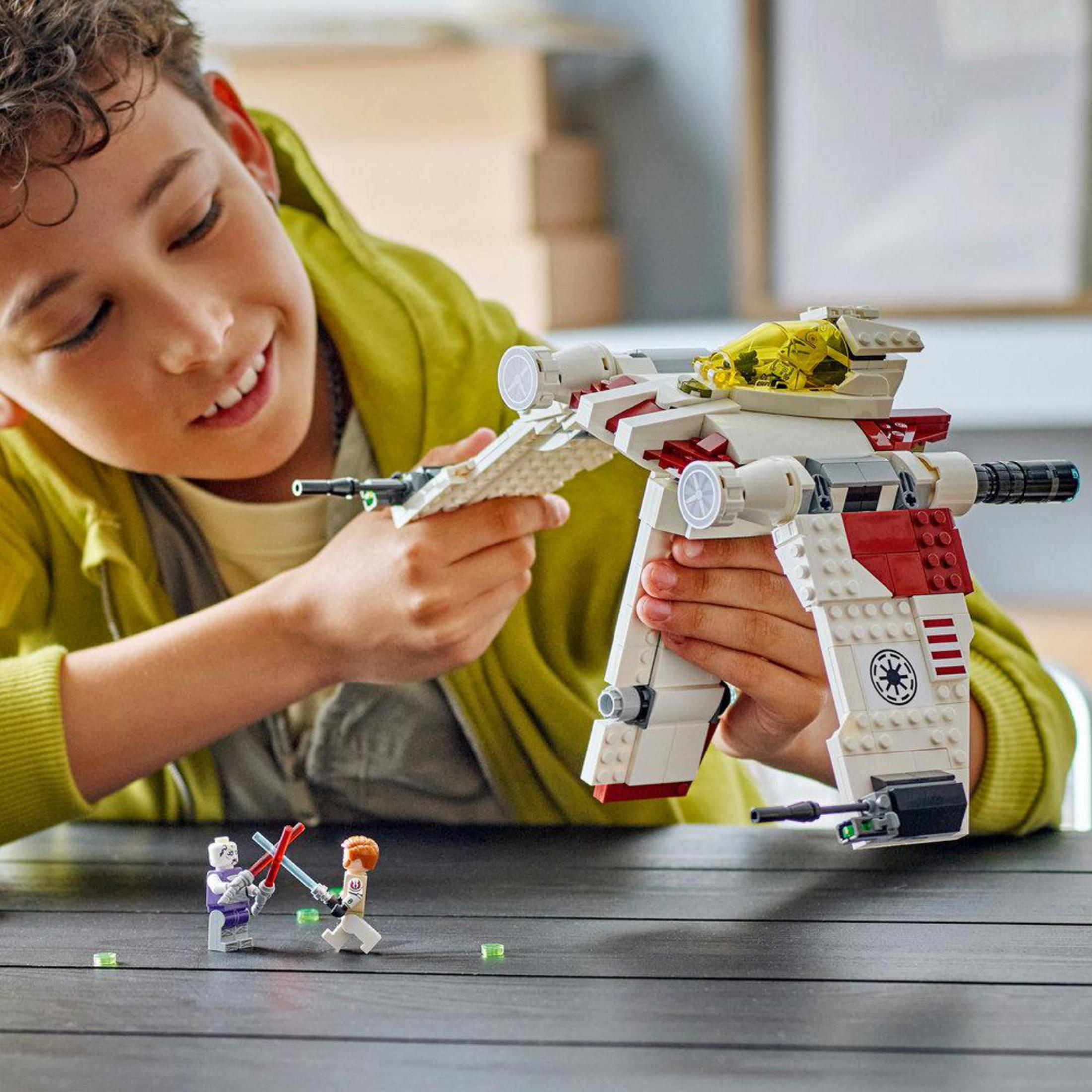 Bir çocuk, ışın kılıçlarıyla savaşan Lego uzay gemisi ve figürleriyle oynuyor.