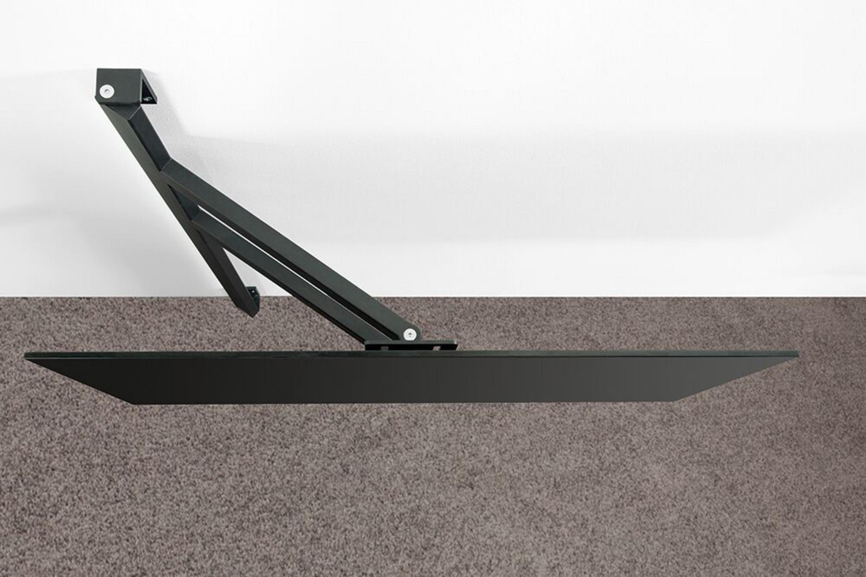 Ein schwarzer Wandregalarm aus Metall mit einer Glasplatte auf einem Teppich.