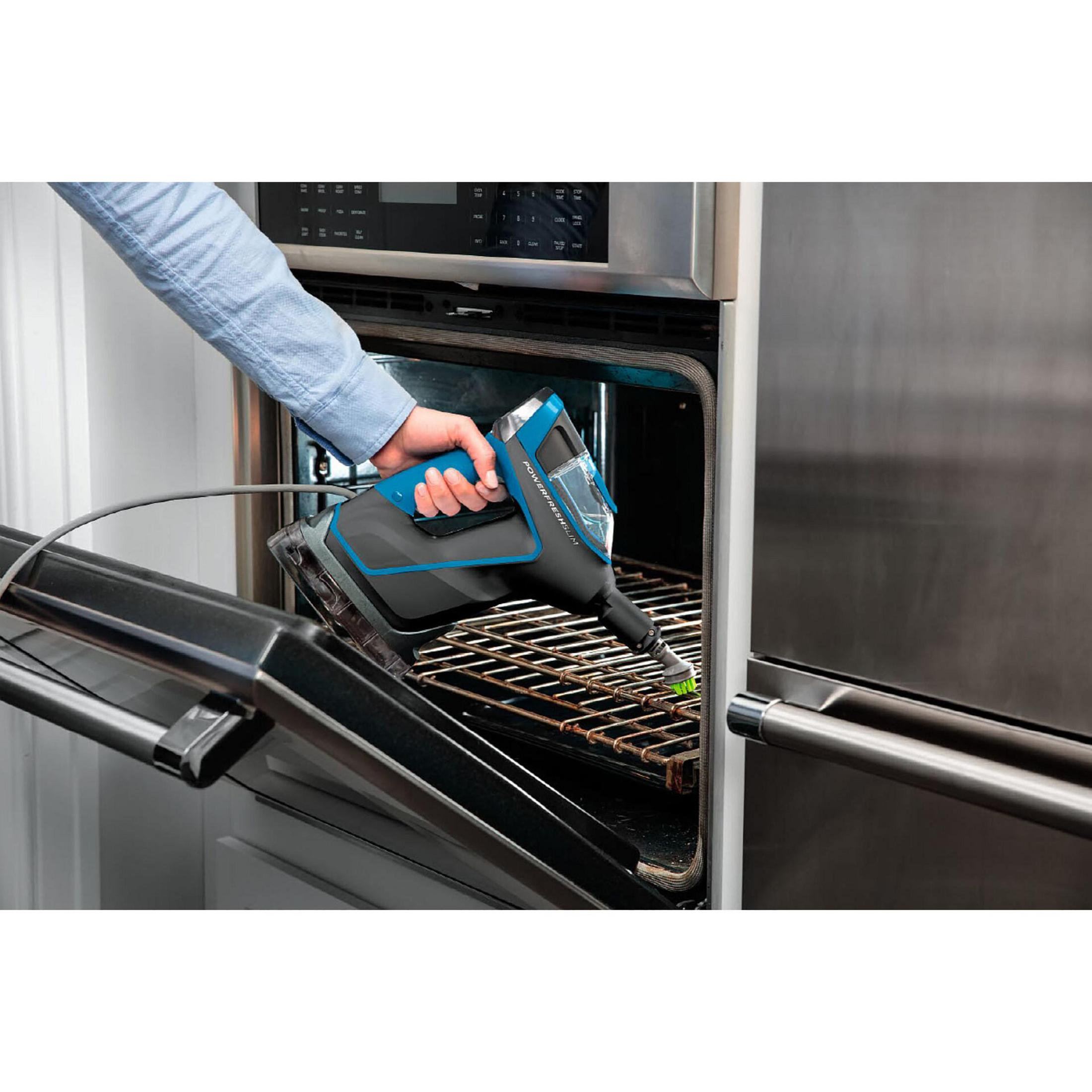 Eine Hand benutzt einen Dampfreiniger, um einen Backofengrill zu reinigen.