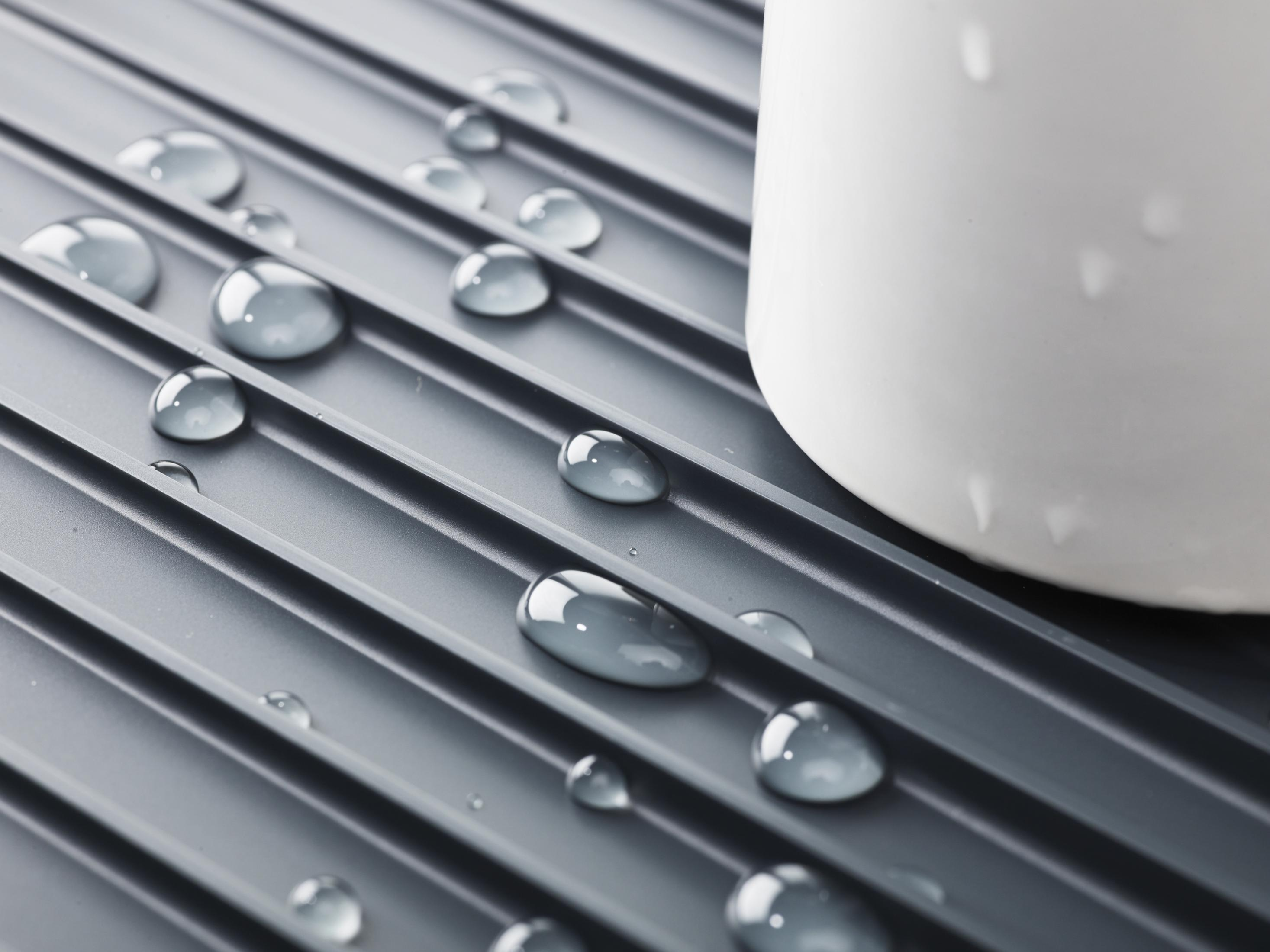 Gotas de agua sobre una superficie acanalada gris junto a una taza blanca.