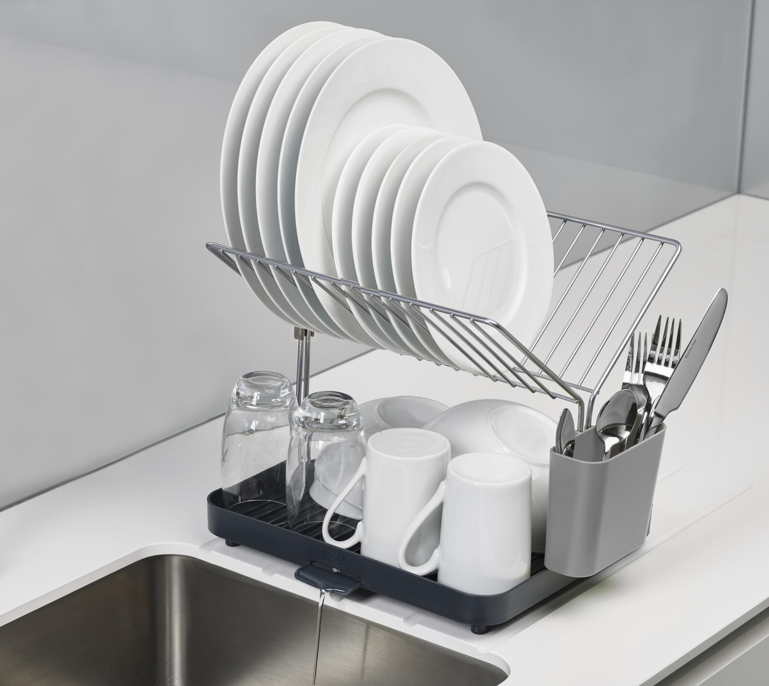 Un escurreplatos sostiene platos blancos limpios, vasos y cubiertos junto a un fregadero.