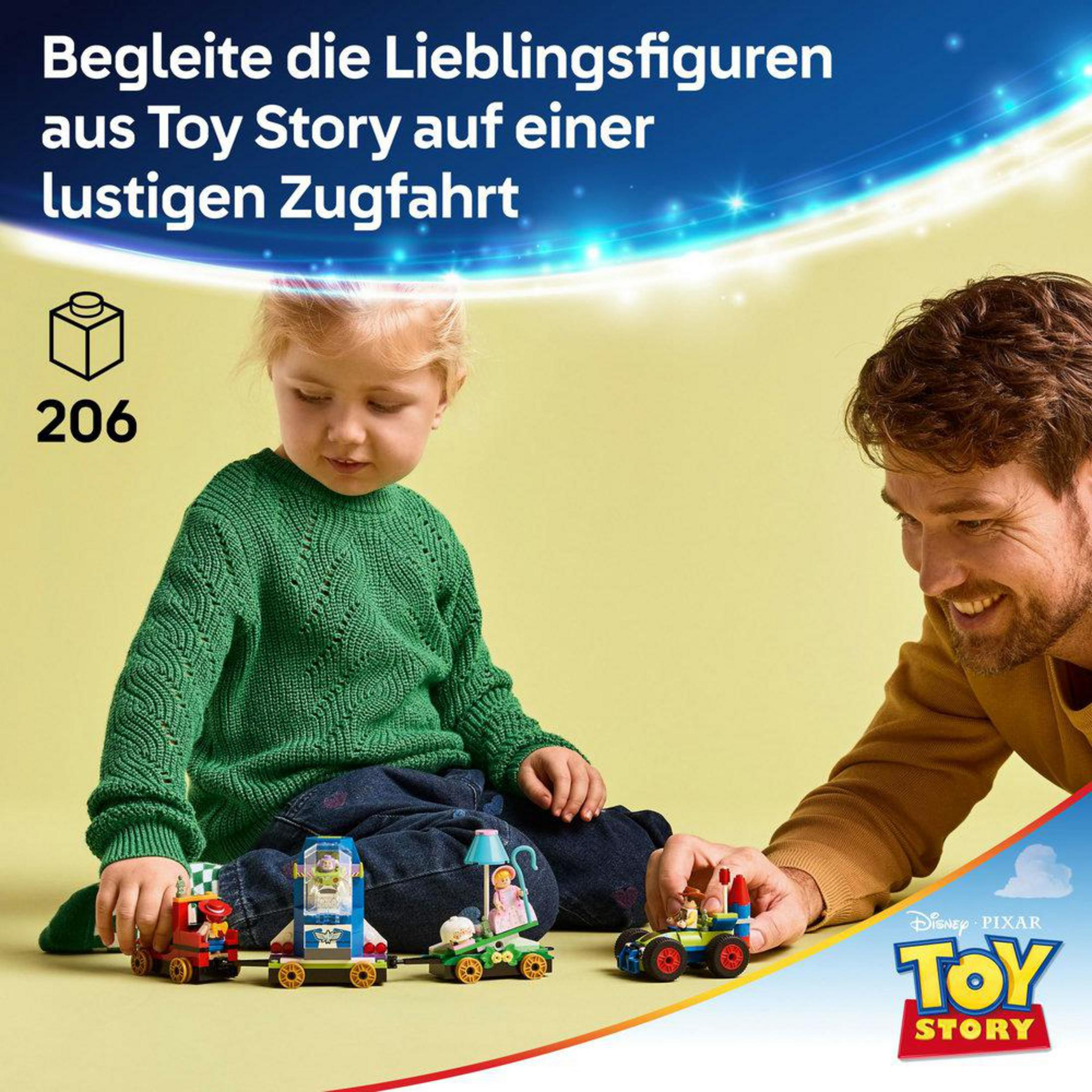 Un niño con suéter verde juega con piezas de tren Lego de Toy Story junto a un hombre sonriente.
