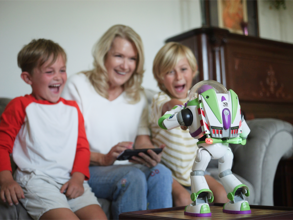 Un juguete de Buzz Lightyear está sobre una mesa mientras ríen dos niños y una mujer.
