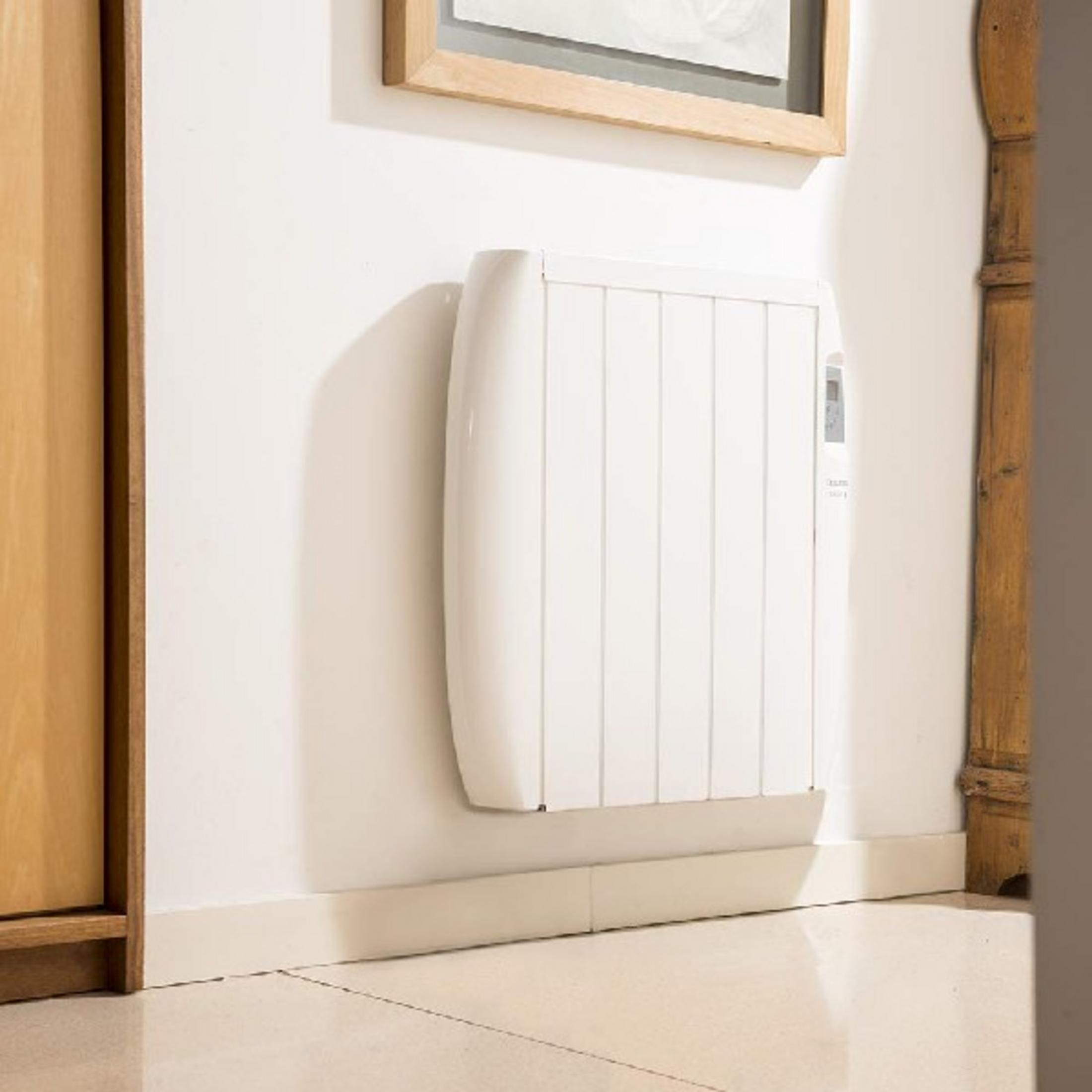 Un termosifone bianco è appeso a una parete bianca accanto a una cornice di legno.