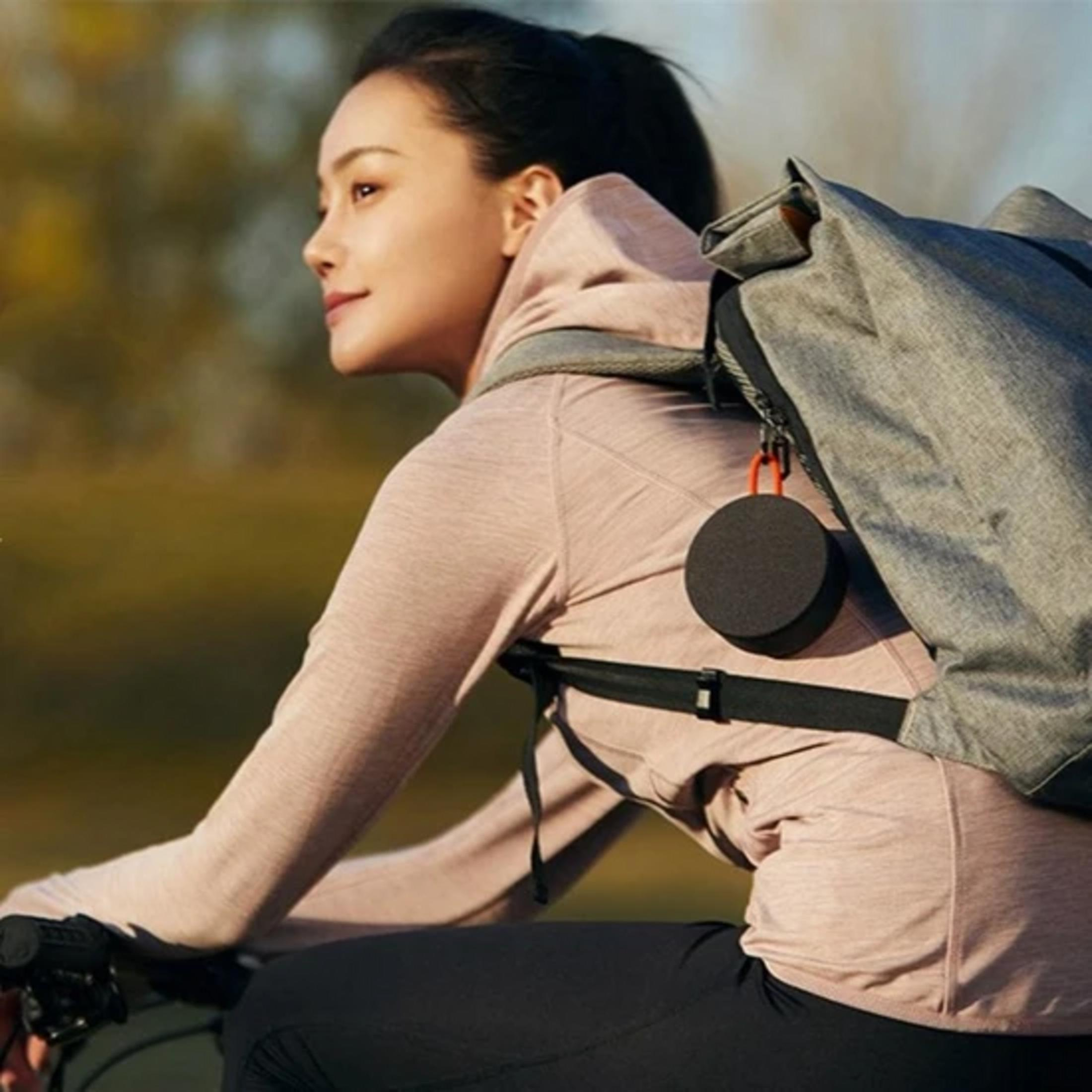 Una donna con zaino va in bicicletta, con un piccolo altoparlante.