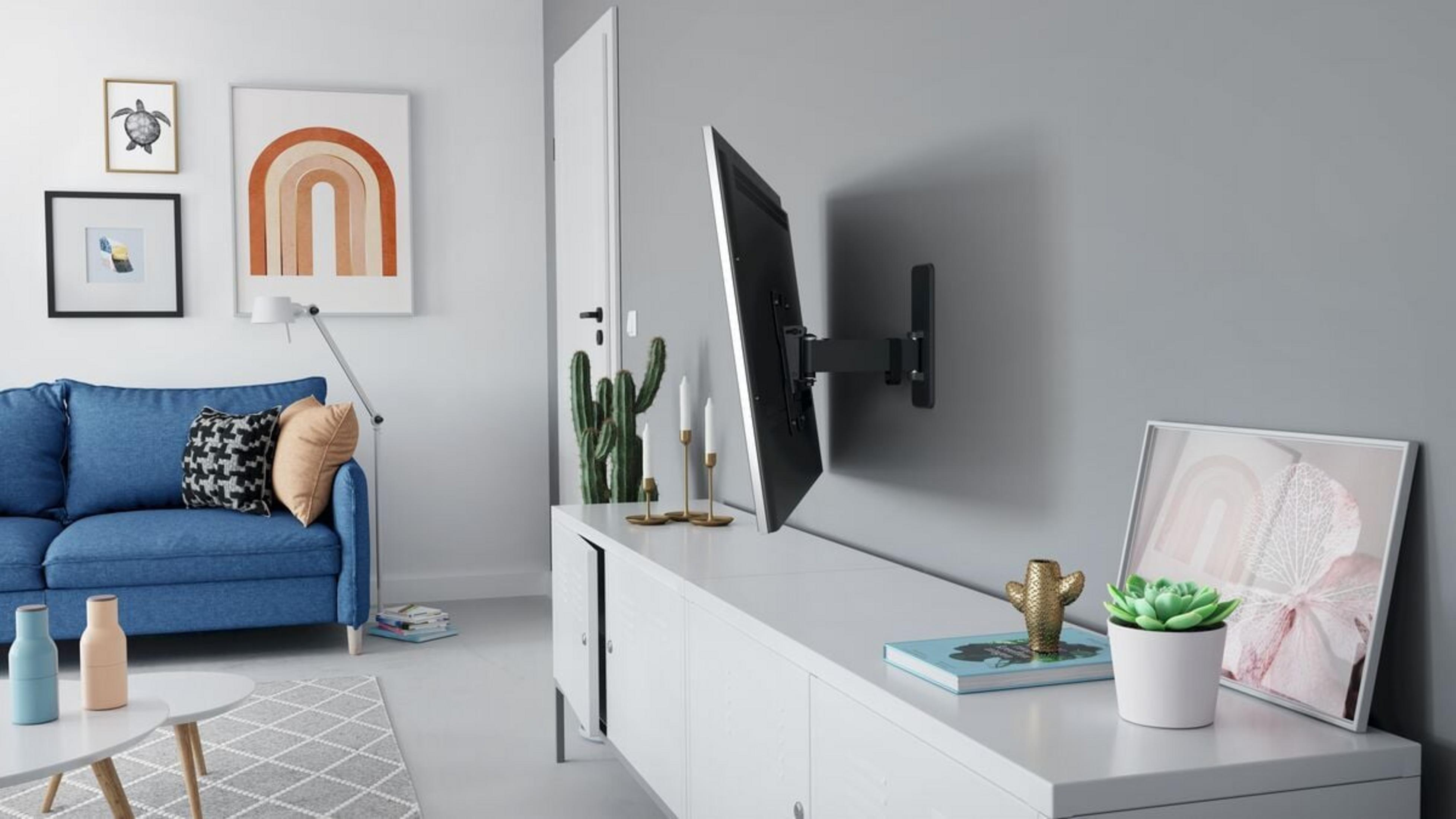 Un soggiorno con divano blu, TV su staffa a muro, credenza, cactus e opere d'arte.