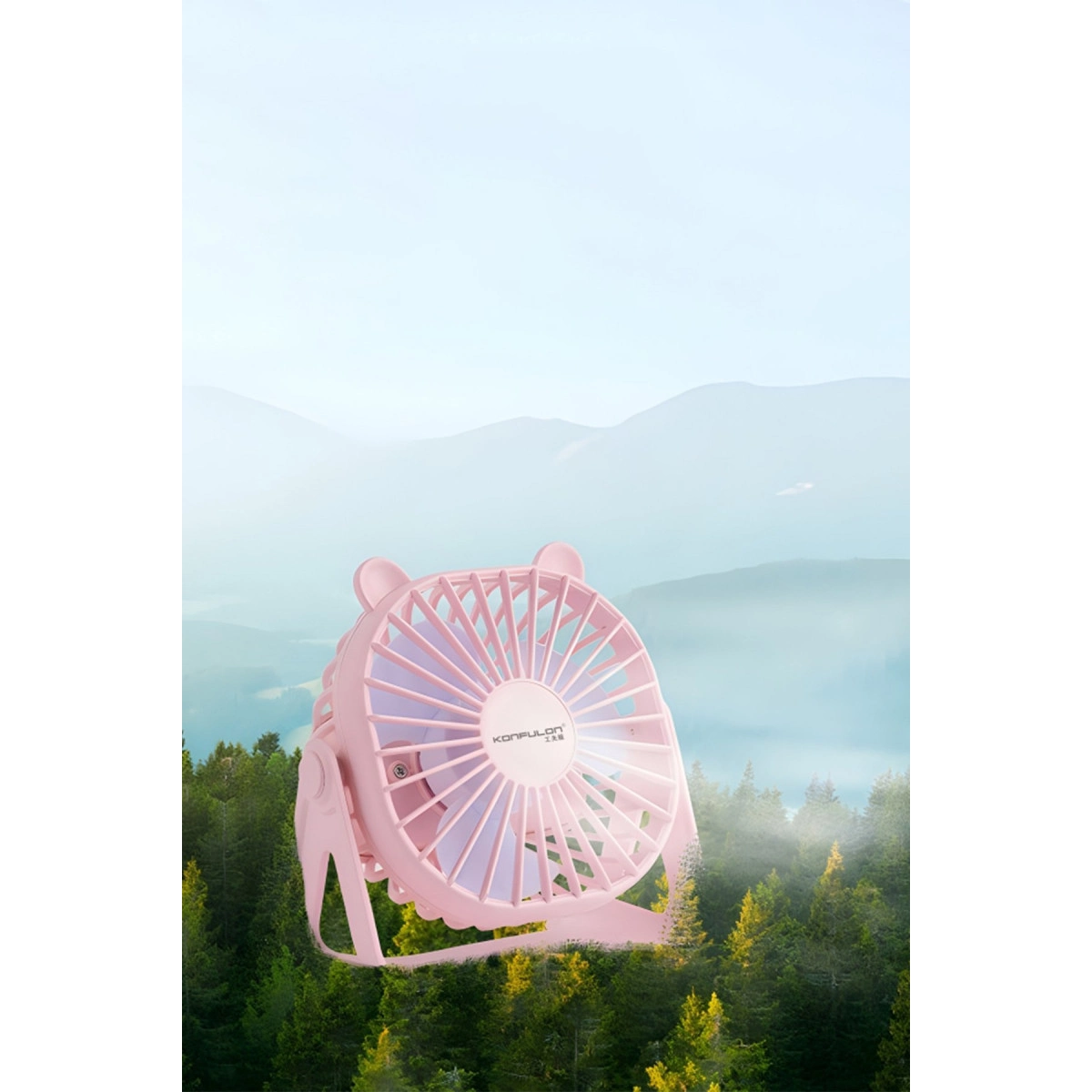 Ayı kulaklı pembe mini vantilatör, ağaçlar ve dağlardan oluşan bulanık bir manzara önünde duruyor.