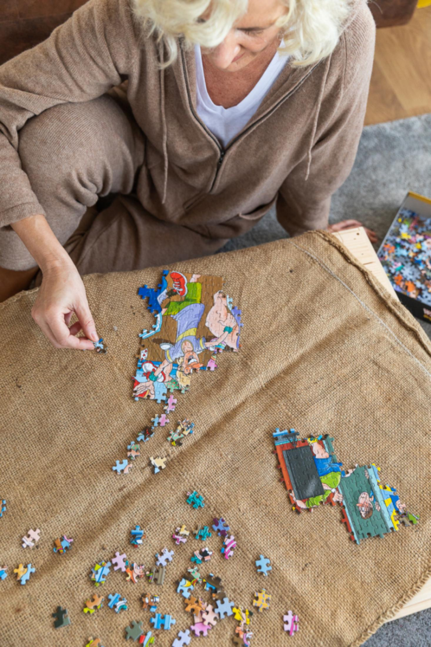 Eine Frau setzt ein buntes Puzzle auf einer Jute-Matte zusammen. Verstreute Teile liegen herum.