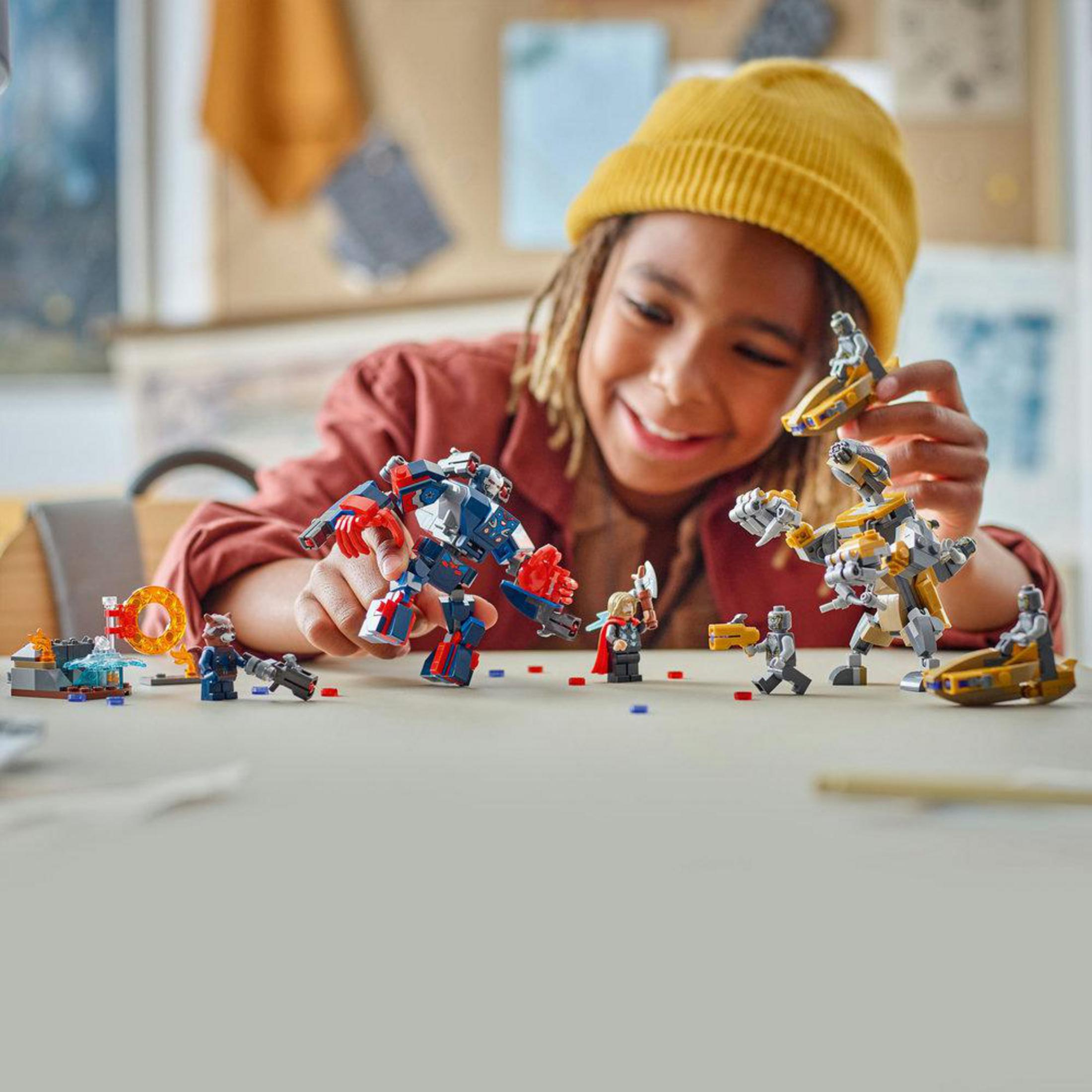 Un bambino gioca con personaggi Lego: un mech blu, un procione e un veicolo giallo.