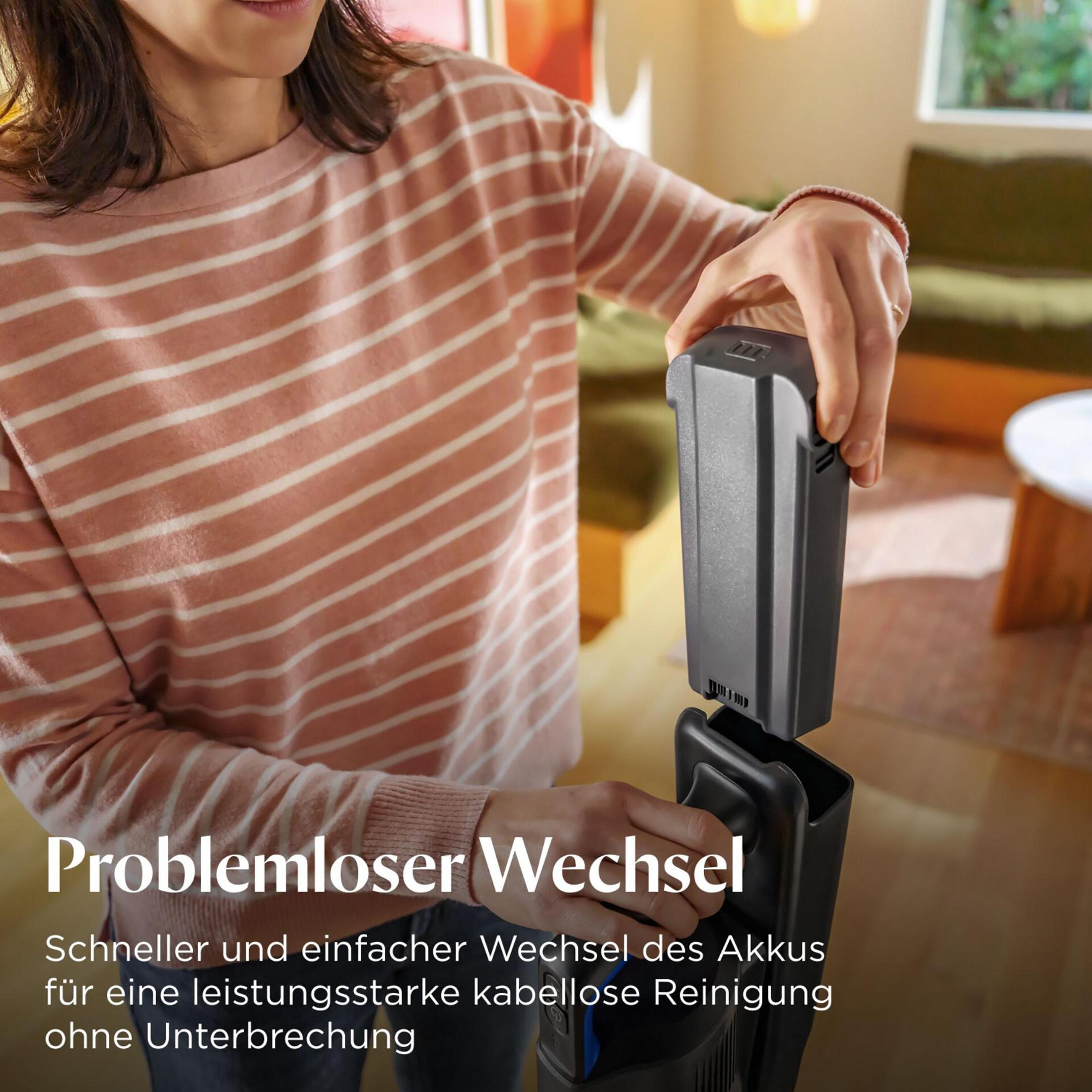 Frau wechselt Akku eines Staubsaugers in einem Wohnzimmer.