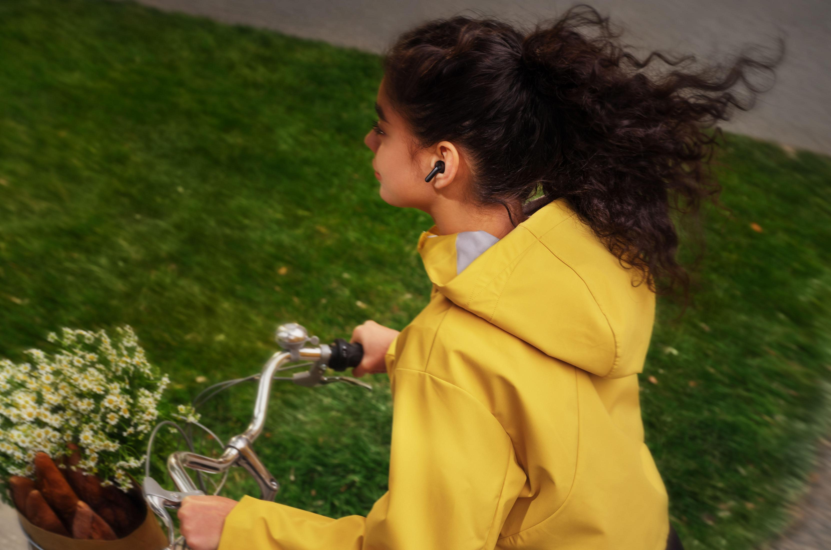 Una ragazza in giacca gialla va in bicicletta. Indossa auricolari.