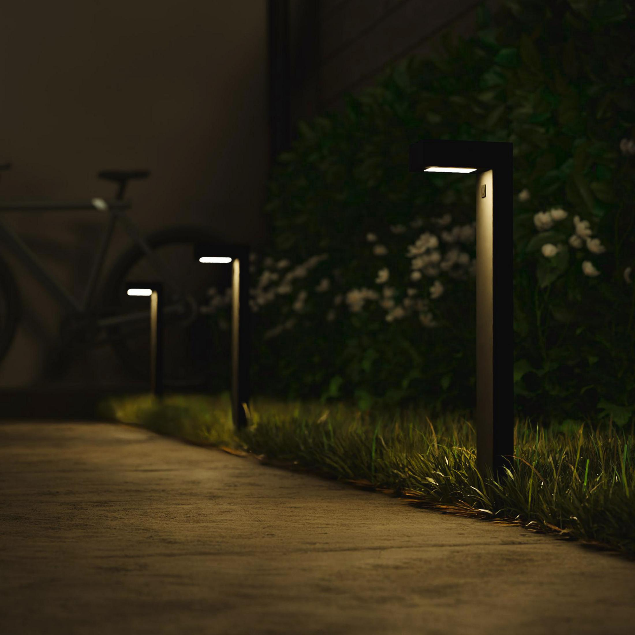 Luces de camino modernas para exteriores iluminan un sendero por la noche, con una bicicleta al fondo.
