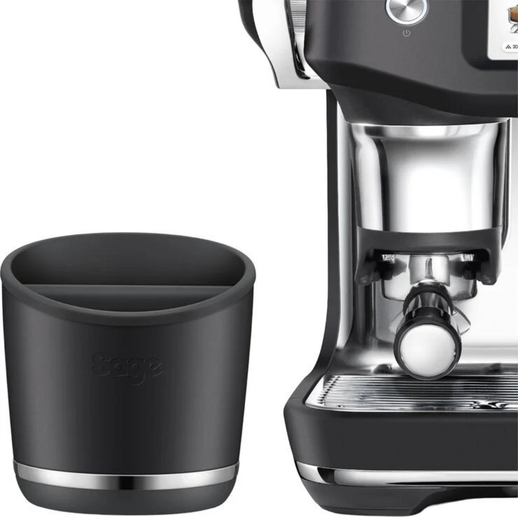 Ein schwarzer Kaffeesatzbehälter neben einer Espressomaschine aus Metall und Schwarz.