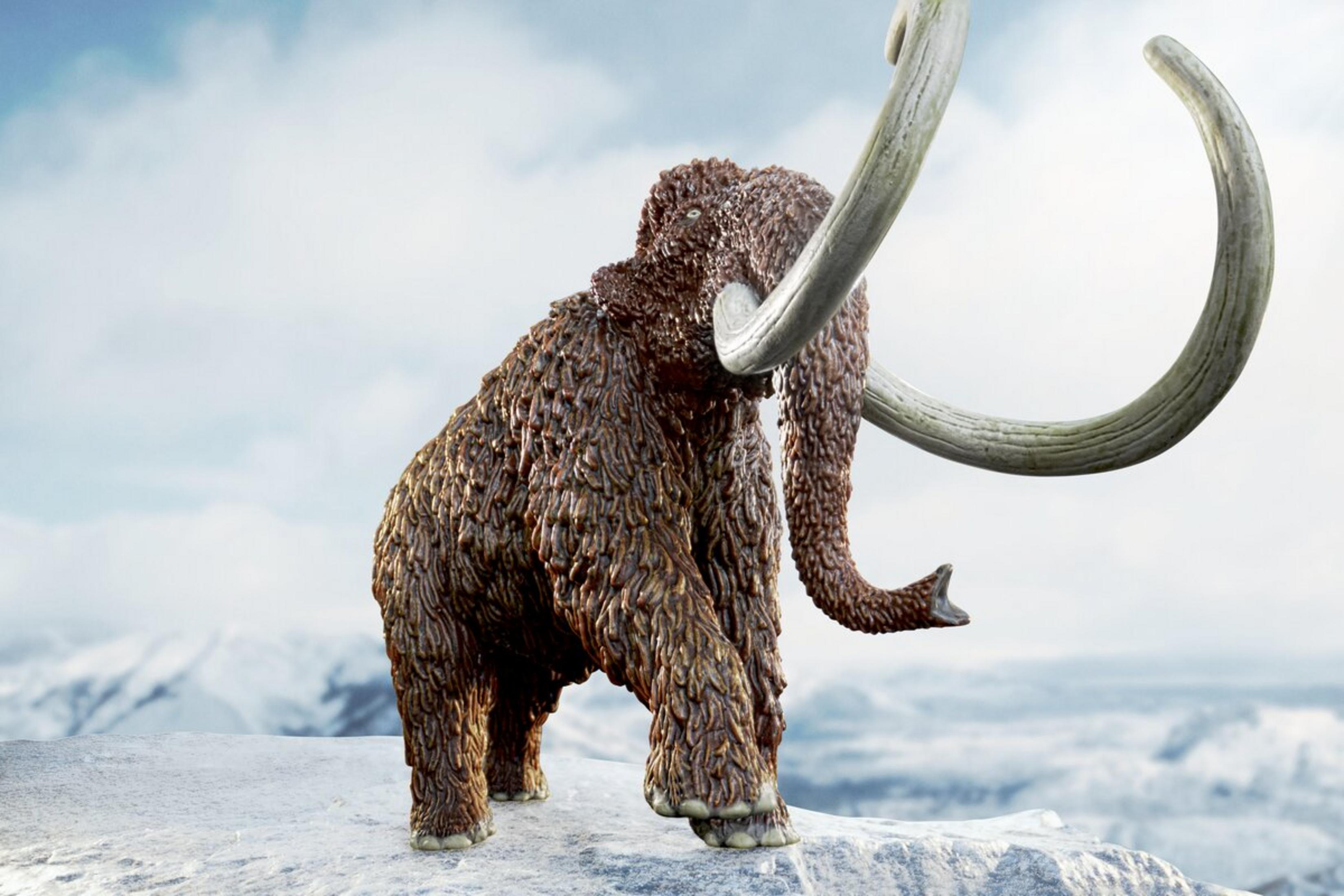 Un mammut lanoso si erge su un terreno innevato davanti a montagne innevate.
