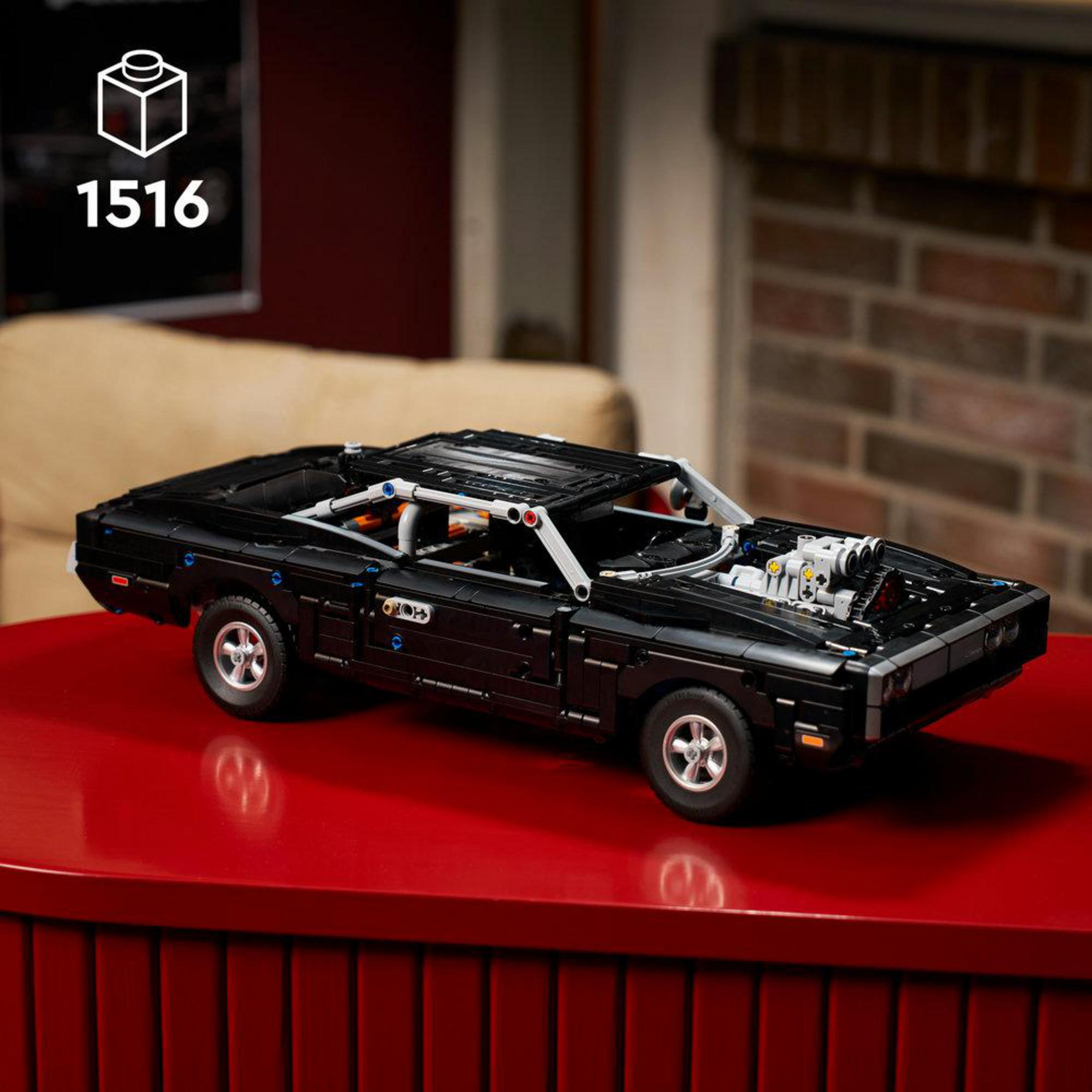 Kaputu açık siyah bir LEGO model araba kırmızı bir masanın üzerinde duruyor.
