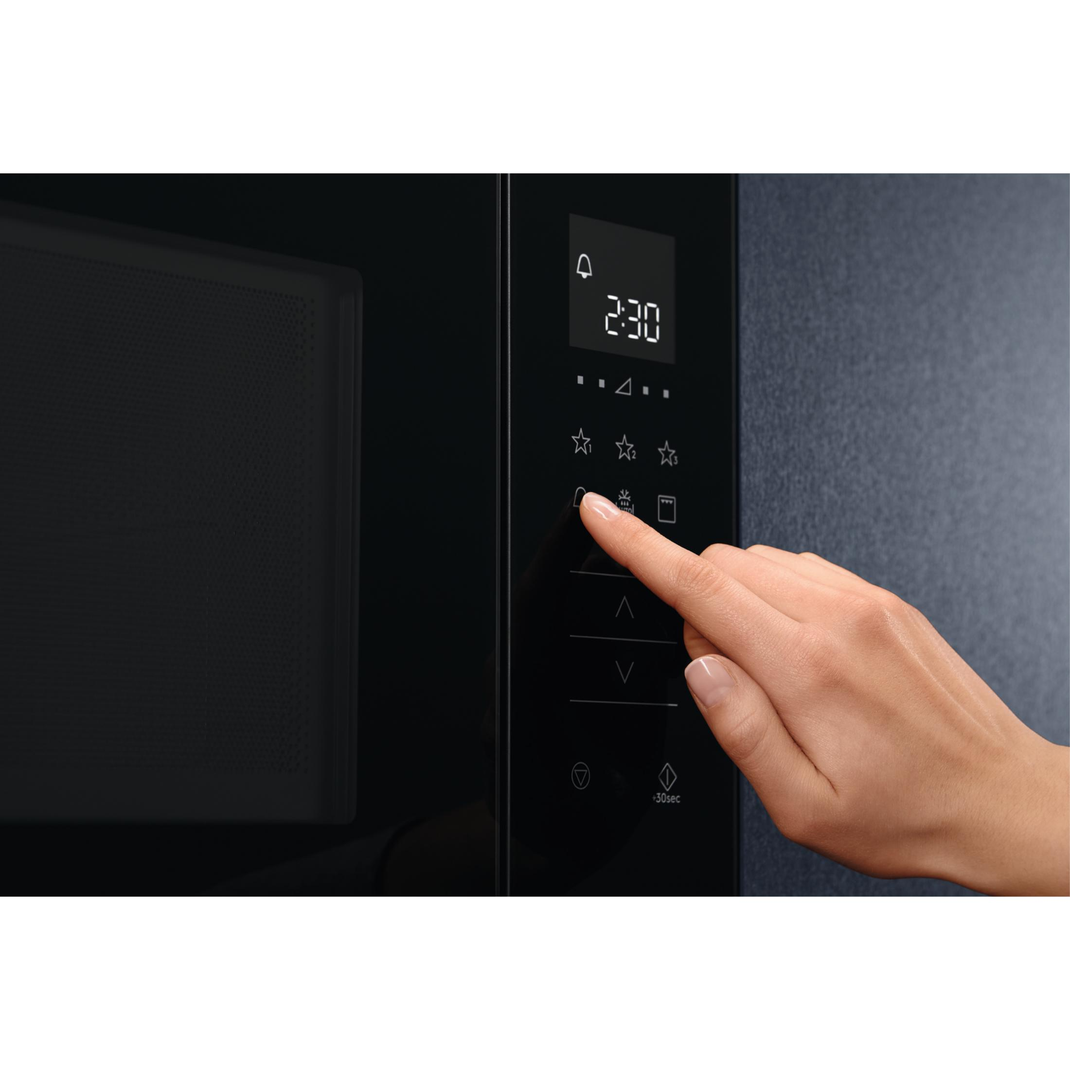 Una mano preme un pulsante sul pannello di controllo di un forno a microonde nero.