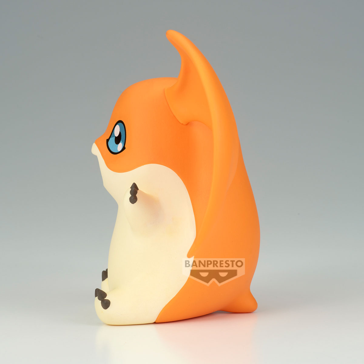 Criatura naranja con ojos azules se sienta mirando a la izquierda. Logo Banpresto visible.