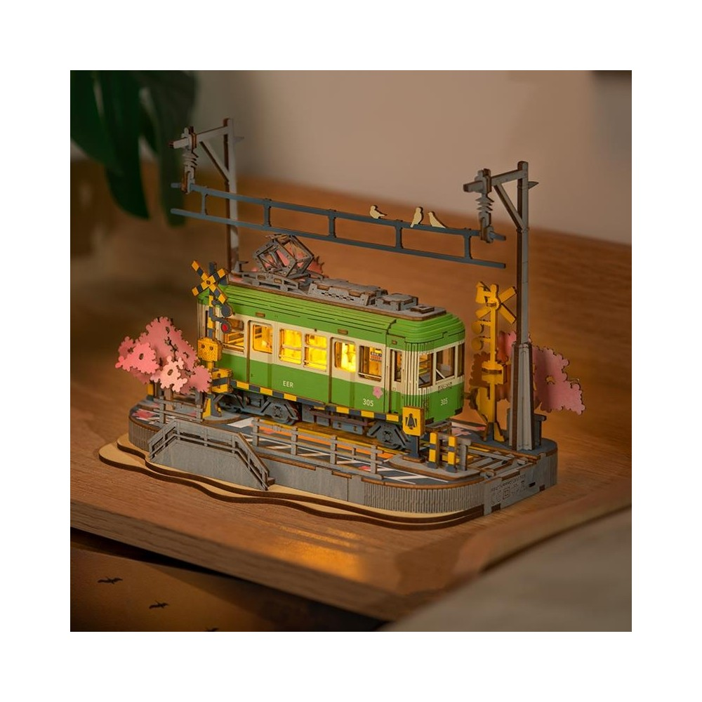 Ein Miniaturmodell einer grünen Straßenbahn mit eingeschalteten Lichtern, auf einem Diorama mit Kirschblüten und Vögeln.