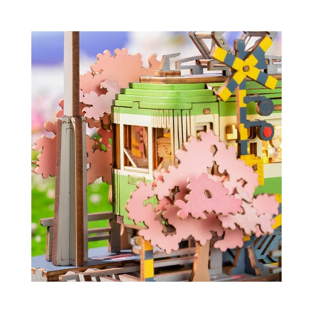 Ein Miniaturmodell einer grünen Straßenbahn mit rosa Kirschblüten und einem Bahnübergangsschild.