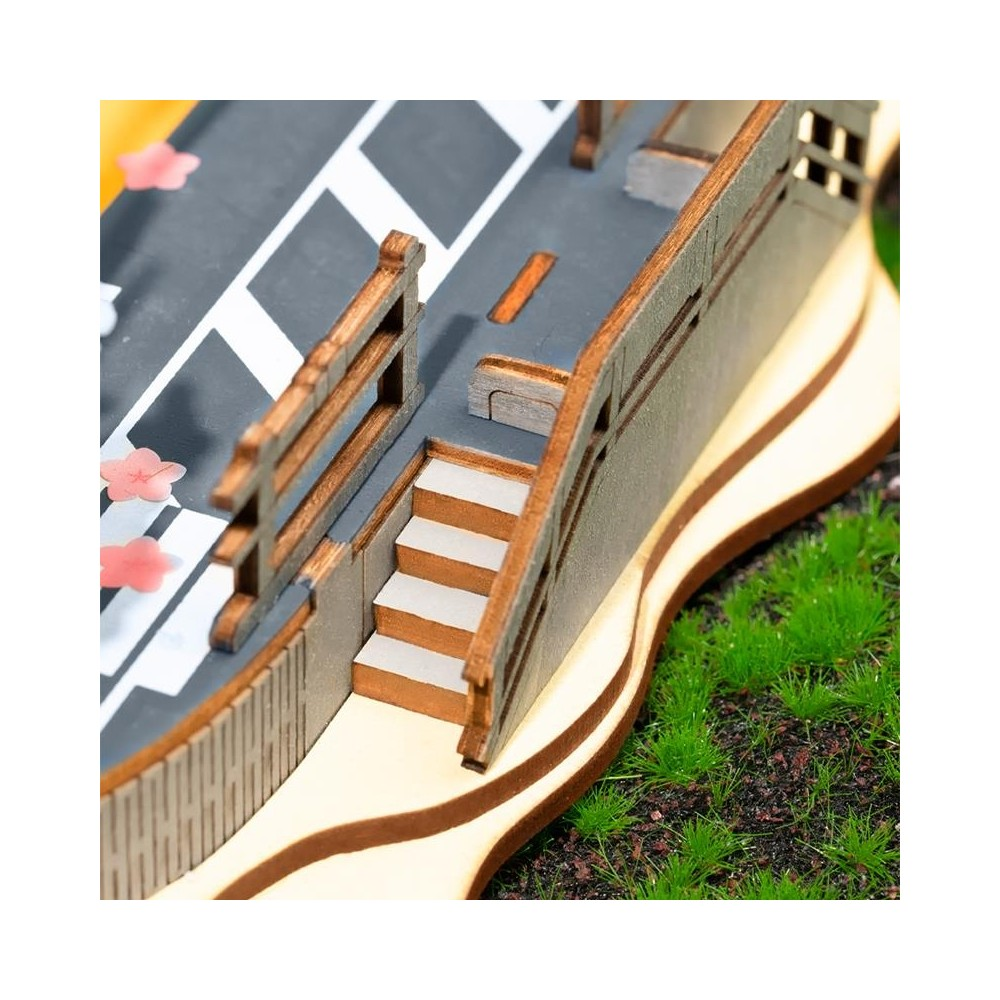 Eine Holzbrücken-Miniatur mit Treppen, Zäunen und rosa Kirschblüten auf einem grauen Weg.