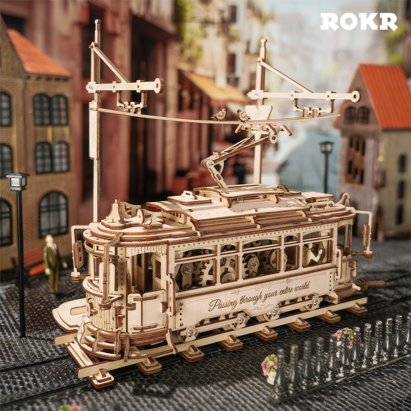 Ein detailliertes Holzmodell einer Straßenbahn auf Schienen mit Gebäuden im Hintergrund.
