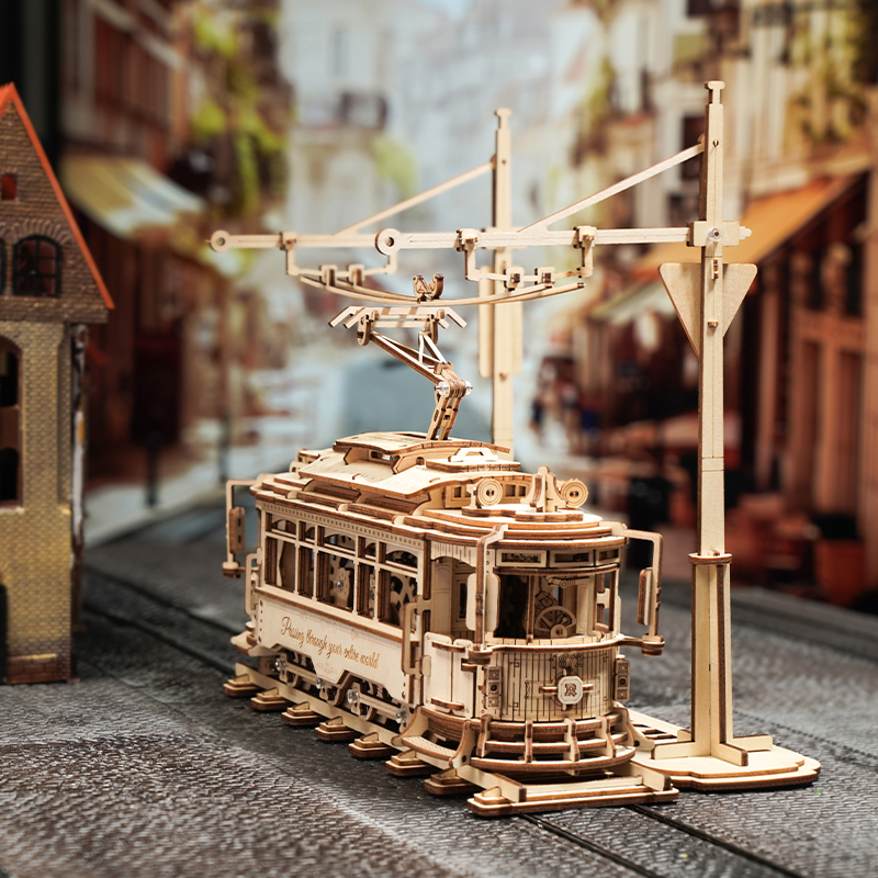 Hölzernes Modell einer Straßenbahn auf Gleisen vor unscharfem Hintergrund einer Stadt.