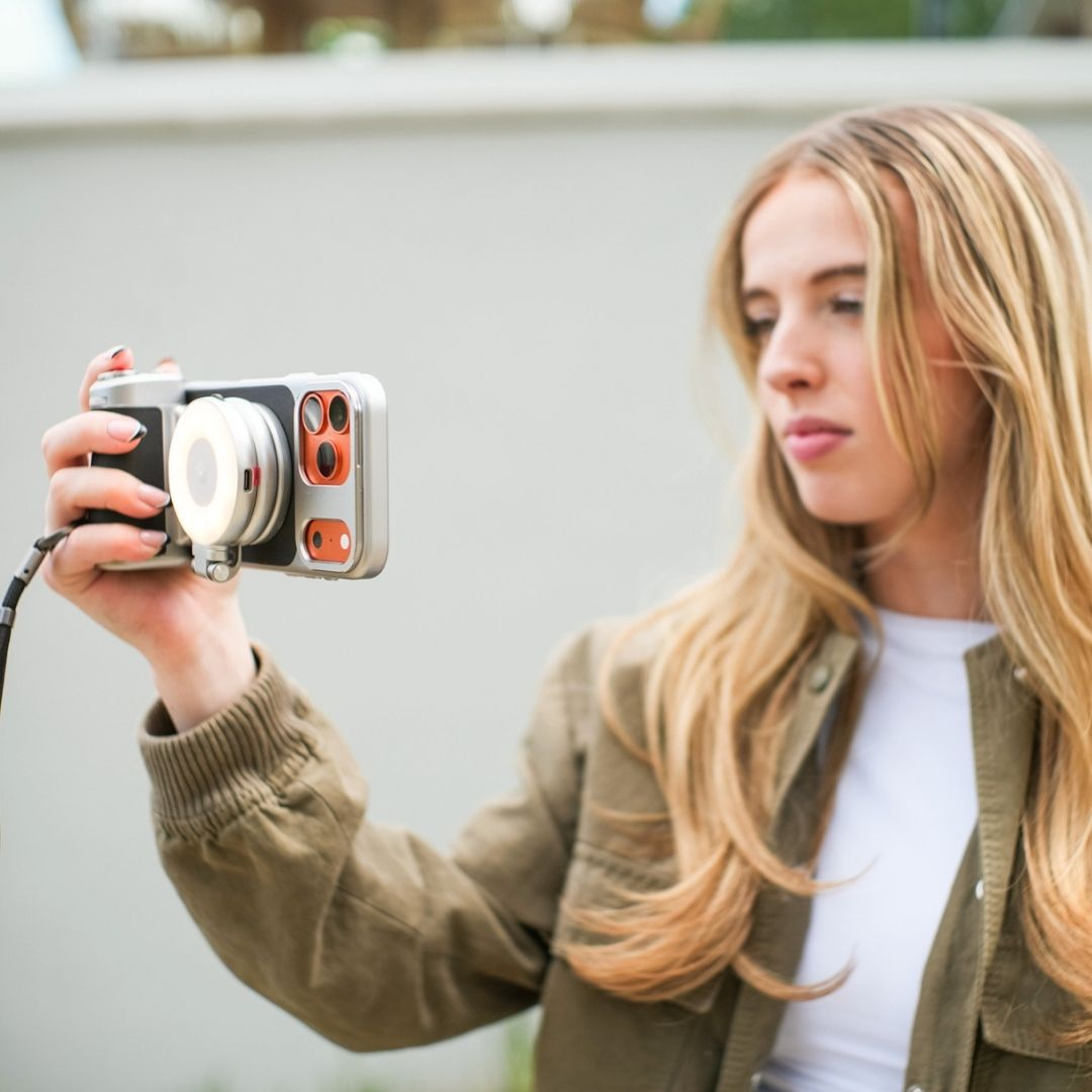 Una giovane donna dai capelli biondi lunghi tiene una fotocamera con luce anulare.