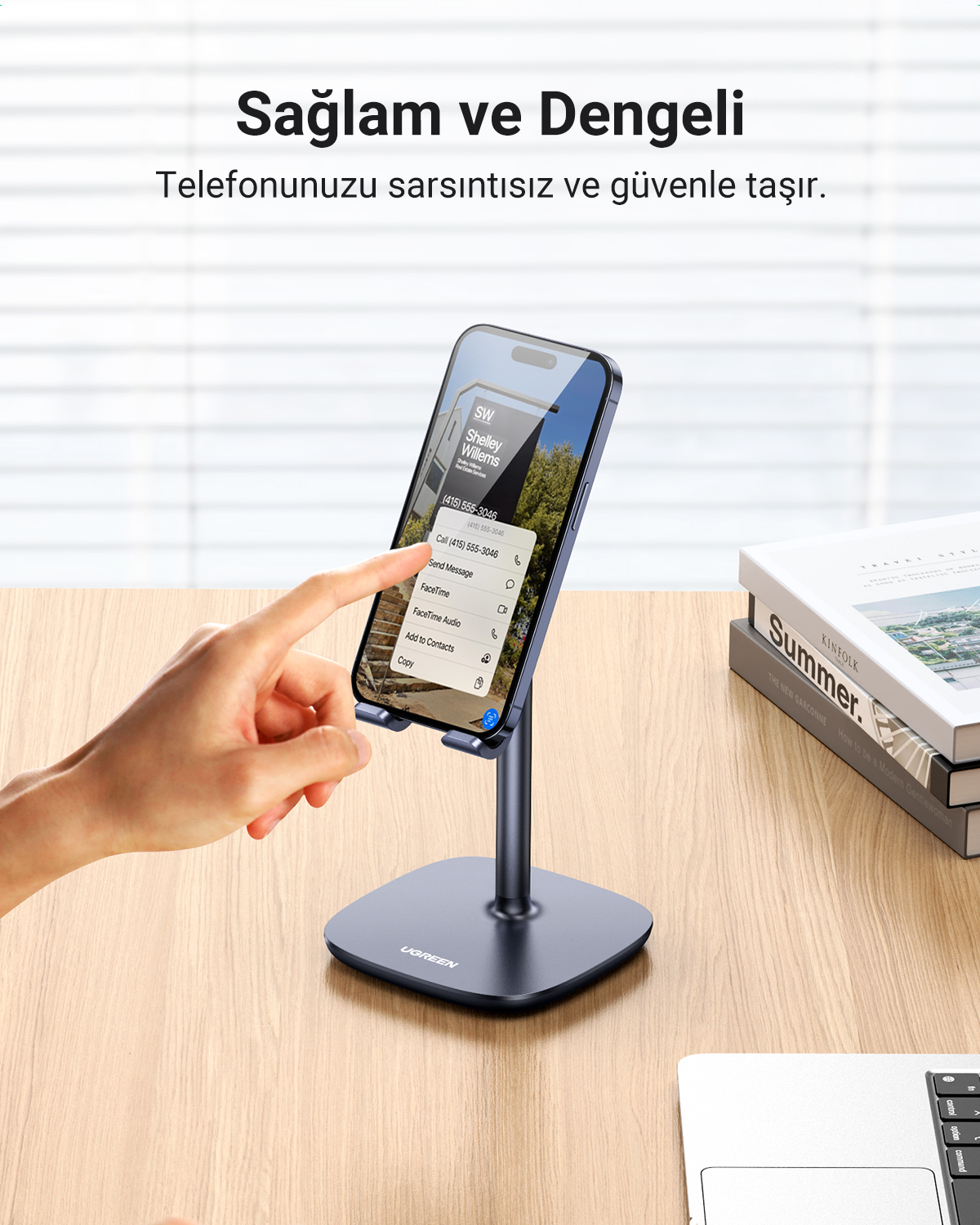 Koyu renkli bir stanttaki akıllı telefona bir el dokunuyor. Yanında kitaplar var.